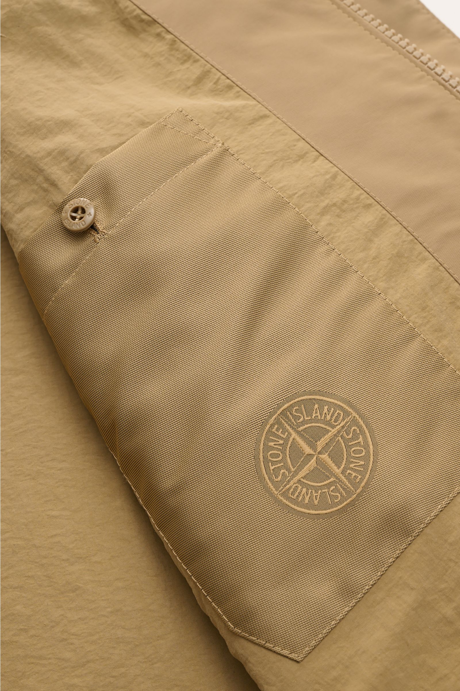 Stone Island Suede jacket 'Ghost Piece' light brown shown in close-up from above, highlighting the textured patch pocket with tonal compass badge and button.  
Casual statement piece with authentic leather craftsmanship: The suede jacket 'Split Leather