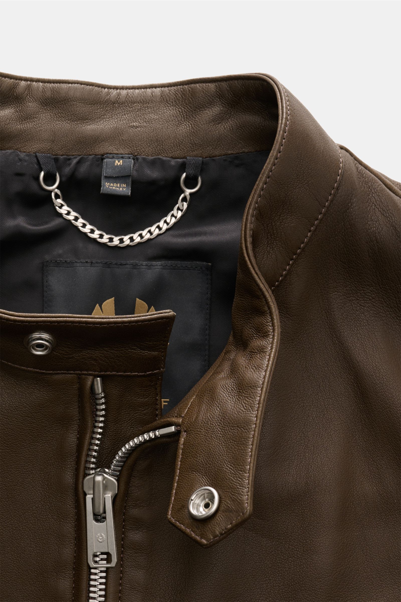 Close-up front view of Belstaff leather jacket 'Track Racer' dark brown, showcasing supple lambskin, slim fit, robust metal zip, narrow standing collar with snap button tab, and smooth black lining with hanging chain. A clean biker look from BELSTAFF: The