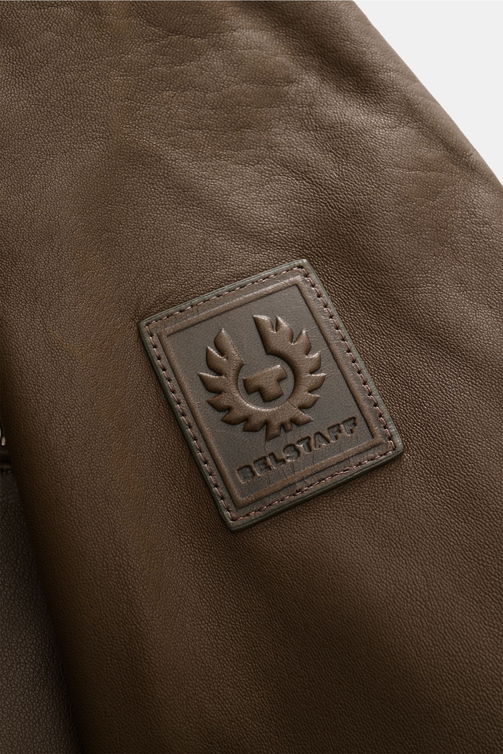 Close-up view of the Belstaff Leather jacket 'Track Racer' dark brown showing the embossed BELSTAFF logo patch on supple lambskin leather, highlighting the modern biker look and fine texture.  

A clean biker look from BELSTAFF: The leather jacket 'Tra