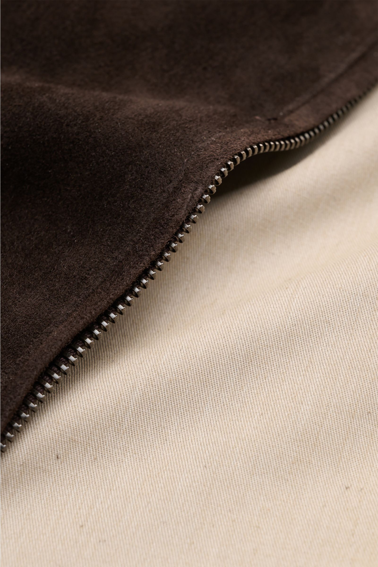Close-up front-side view of the Agnona Suede blouson dark brown showing premium smooth suede material, metal zipper teeth, and contrasting beige cotton-silk lining, highlighting the slim fit, high-closing collar, patch pockets with buttons, elasticated ri