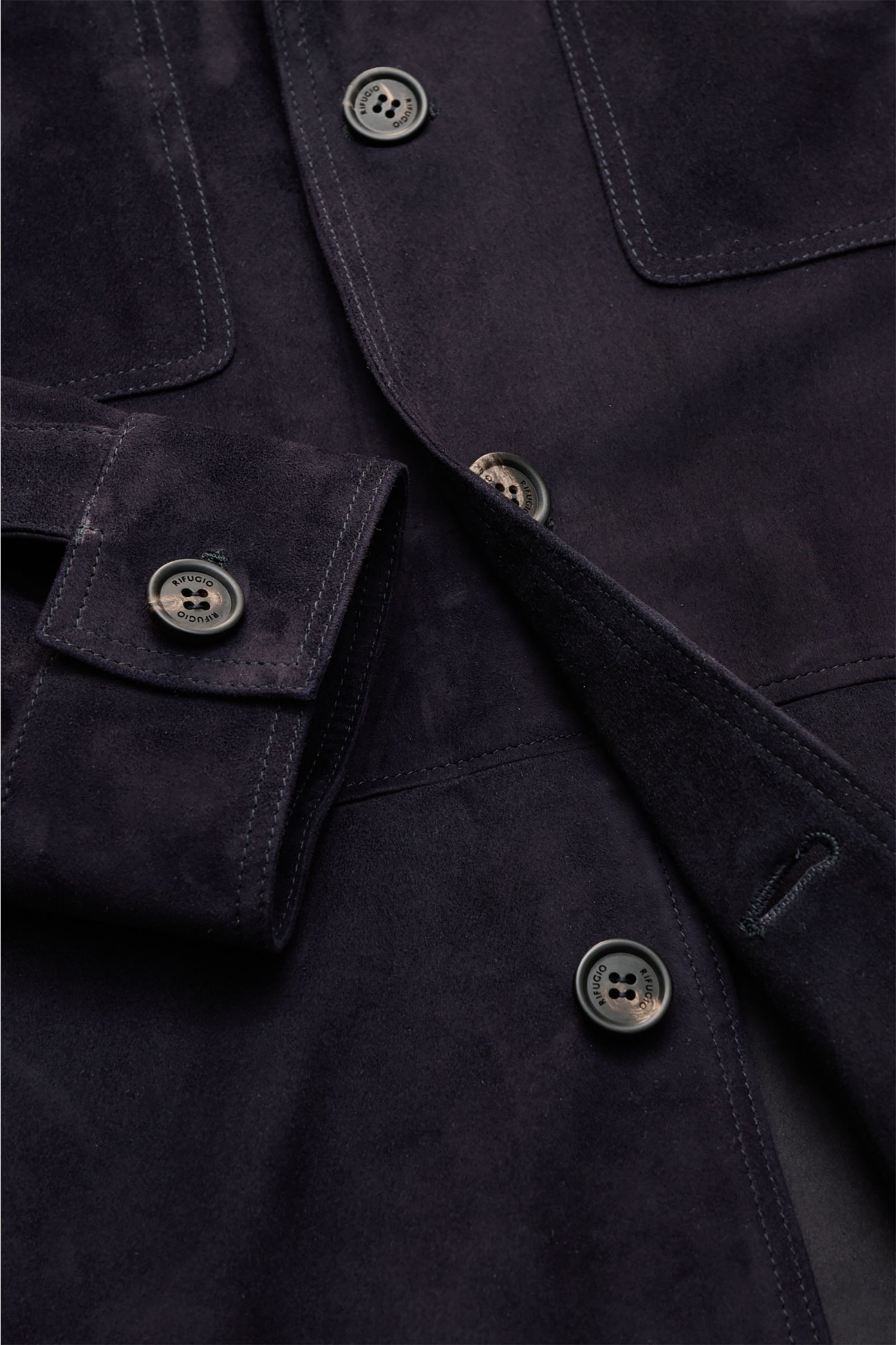 Nahaufnahme der Rifugio Velourslederjacke schwarz von oben, Fokus auf samtiges Veloursleder, Slim Fit, Knöpfe mit Logo, Manschetten und Taschen.