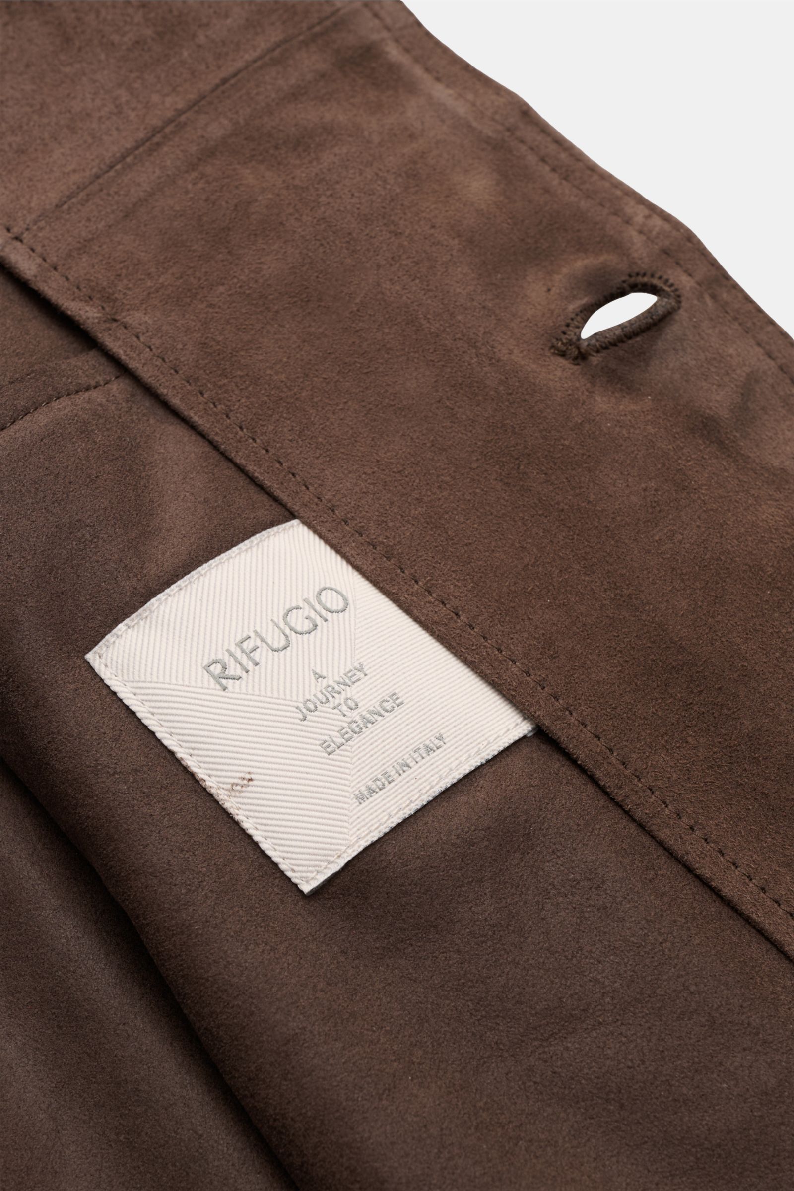 Close-up interior view of the Rifugio Suede jacket dark brown showing supple suede, fine stitching, and the label 'RIFUGIO A Journey to Elegance Made in Italy.' A statement in the finest leather craftsmanship: This suede jacket by RIFUGIO has a velvety so