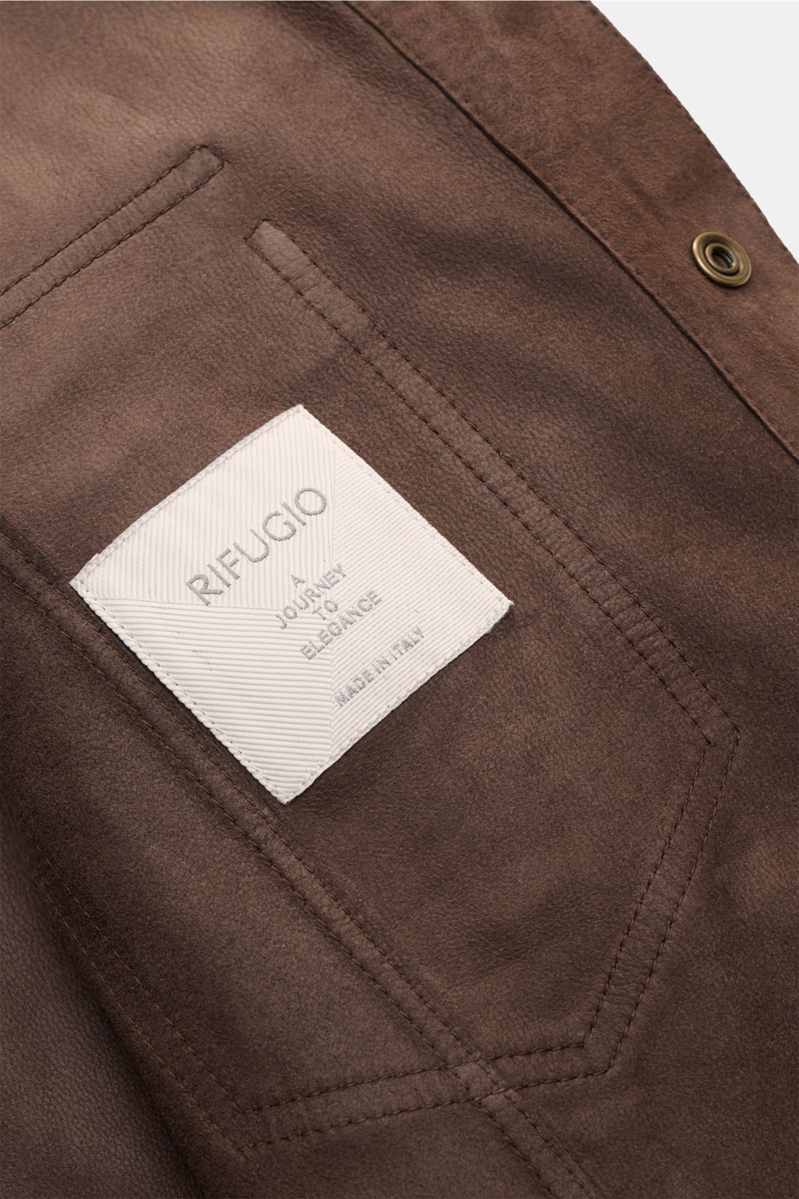 Nahaufnahme der Rifugio Velourslederjacke dunkelbraun von schräg oben, zeigt feines Lammvelours, Brusttasche mit weißem Label und Druckknopf.