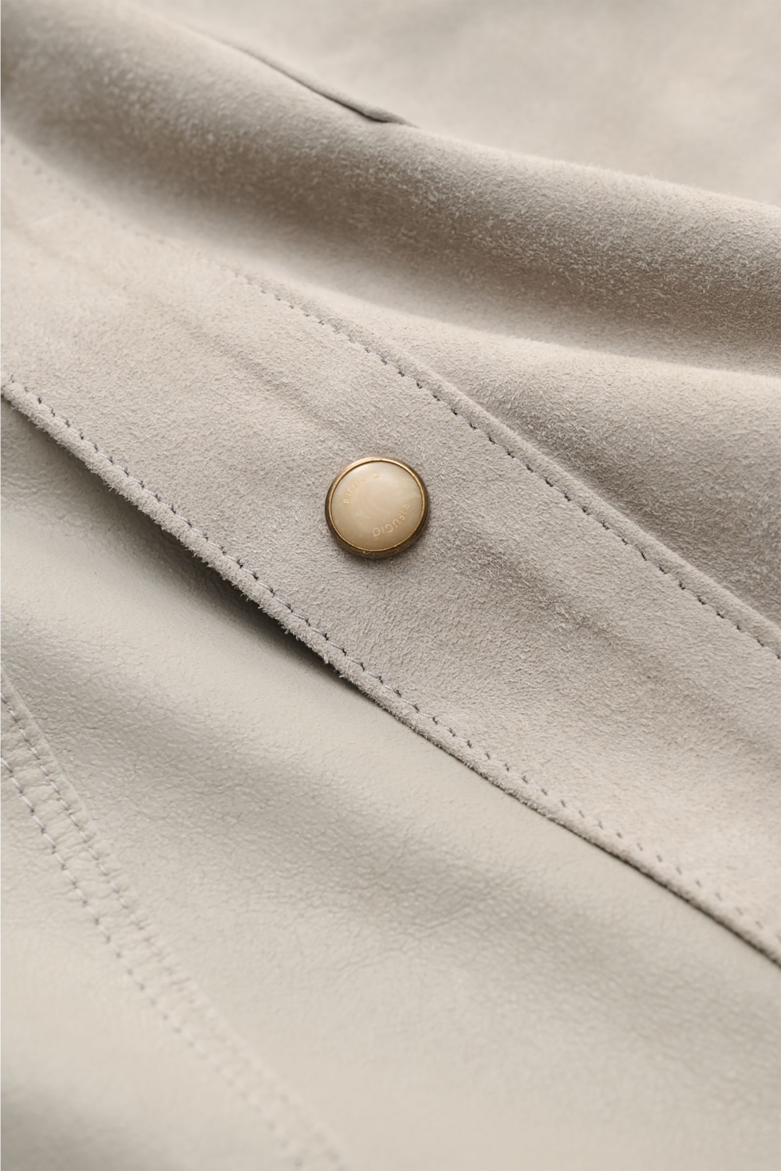 Nahaufnahme aus schräger Perspektive der Rifugio Velourslederjacke hellgrau aus weichem Lammvelours mit Druckknopf und sichtbarer Naht.