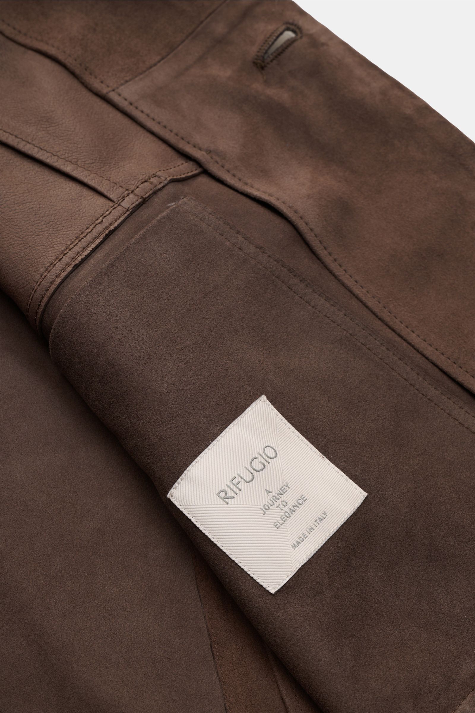 Close-up view of the inside of the Rifugio Suede jacket dark brown showing soft supple suede, fine stitching, and the brand label 'RIFUGIO A JOURNEY TO ELEGANCE MADE IN ITALY,' highlighting its luxurious craftsmanship and unconstructed design.