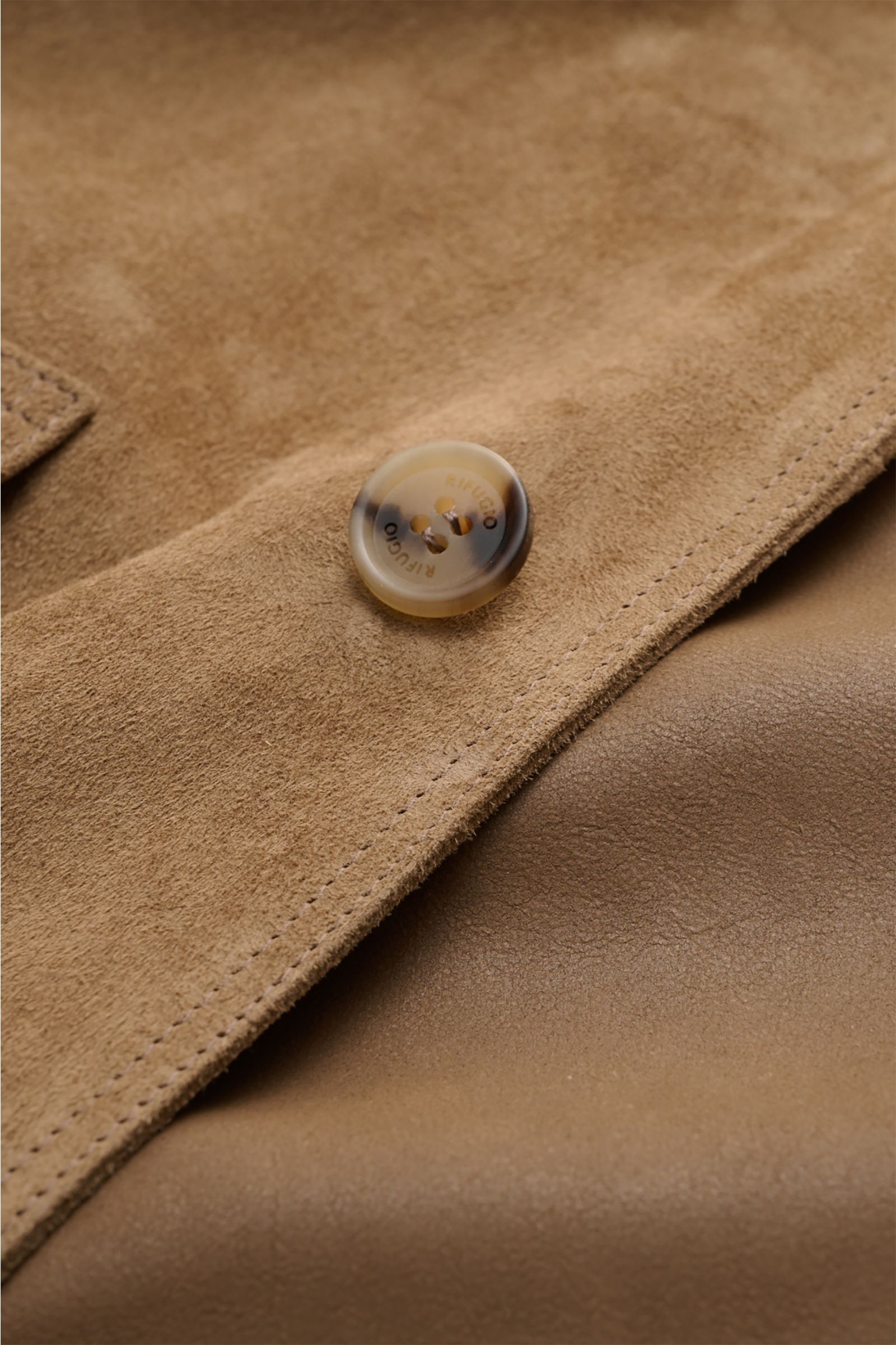 Nahaufnahme der Rifugio Velourslederjacke hellbraun, Detailfoto von samtig-weichem Veloursleder und Knopf mit Logo, weicher Griff sichtbar.