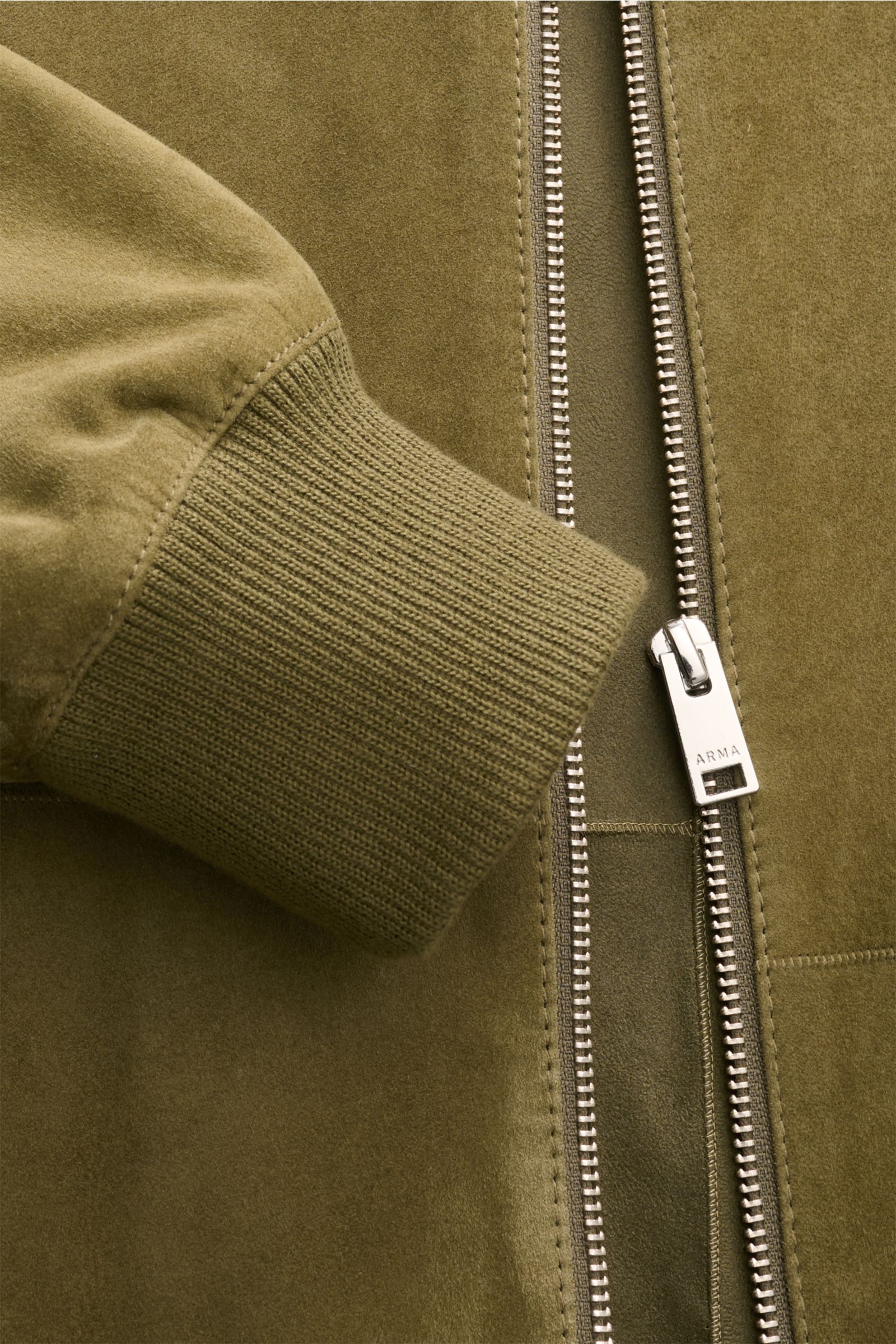 Close-up front view of the Arma Veloursleder-Blouson 'Dion' oliv showing olive green fine goat suede, elastic ribbed cuff, and sturdy two-way zipper. 

Leicht und zeitlos: Der ungefütterte Lederblouson 'Dion' von ARMA ist aus geschmeidigem Ziegenvelour