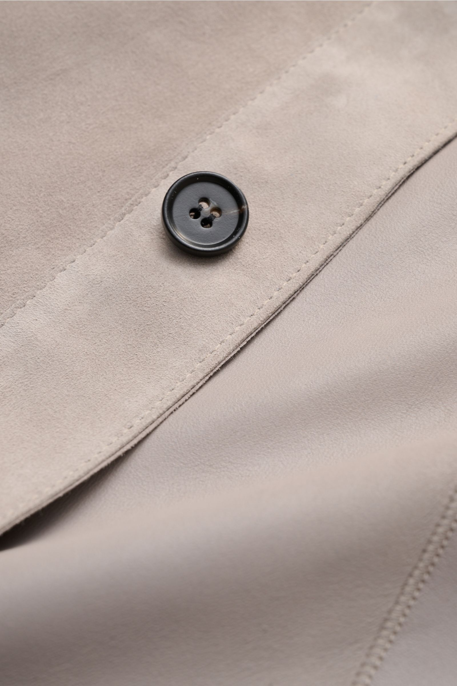 Close-up image of the Arma Velourslederjacke 'Dino' hellgrau showing soft velours leather, a black four-hole button, and fine stitching from a top-down perspective.