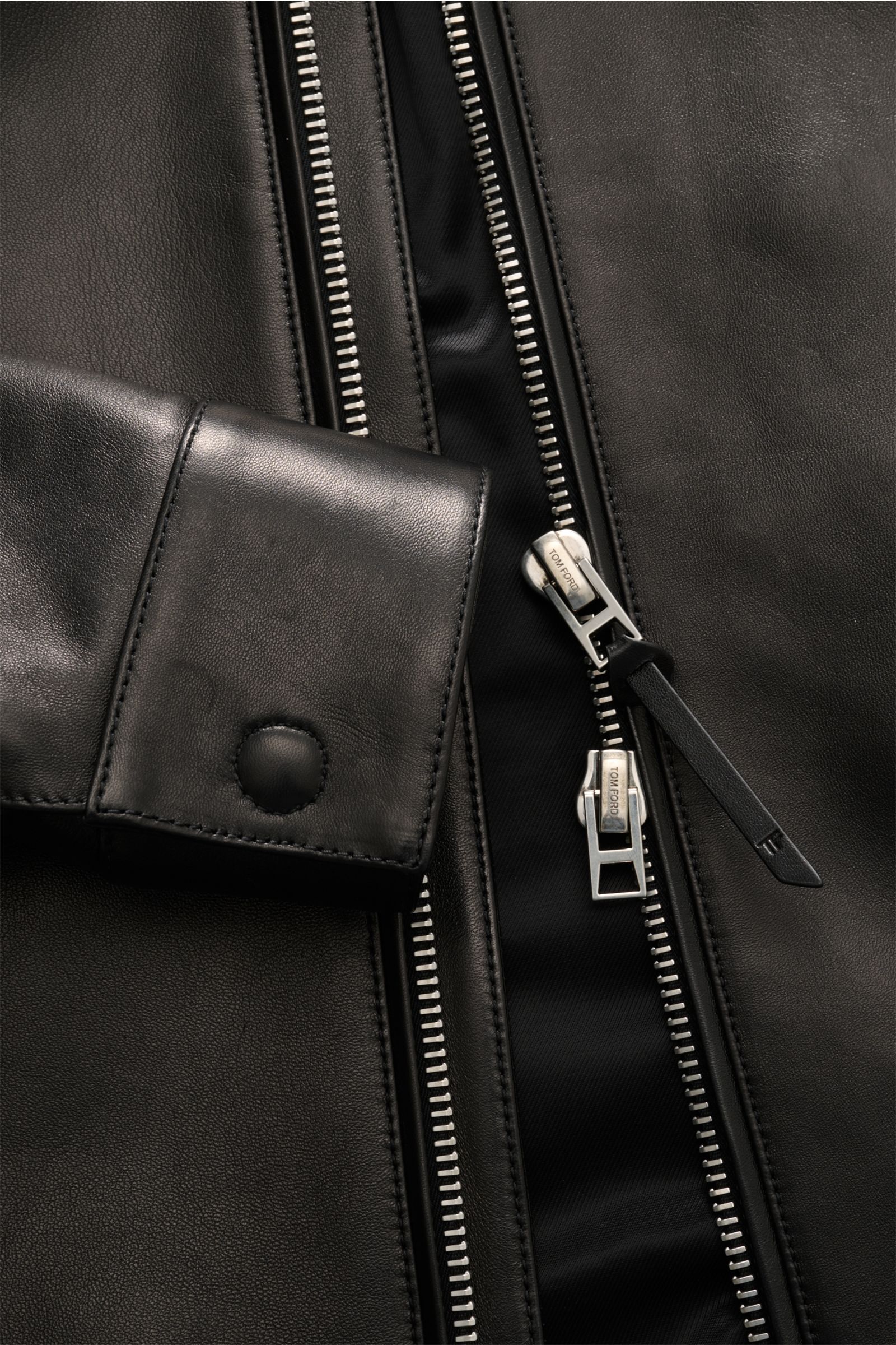 Close-up front view of Tom Ford Lederjacke schwarz showing smooth lamb leather, silver zipper, cuff with button, and soft lining.

Luxus wie gewohnt von TOM FORD: diese Jacke aus geschmeidigem Lammleder mit Umlegekragen wurde in zeitlosem, geradlinigem
