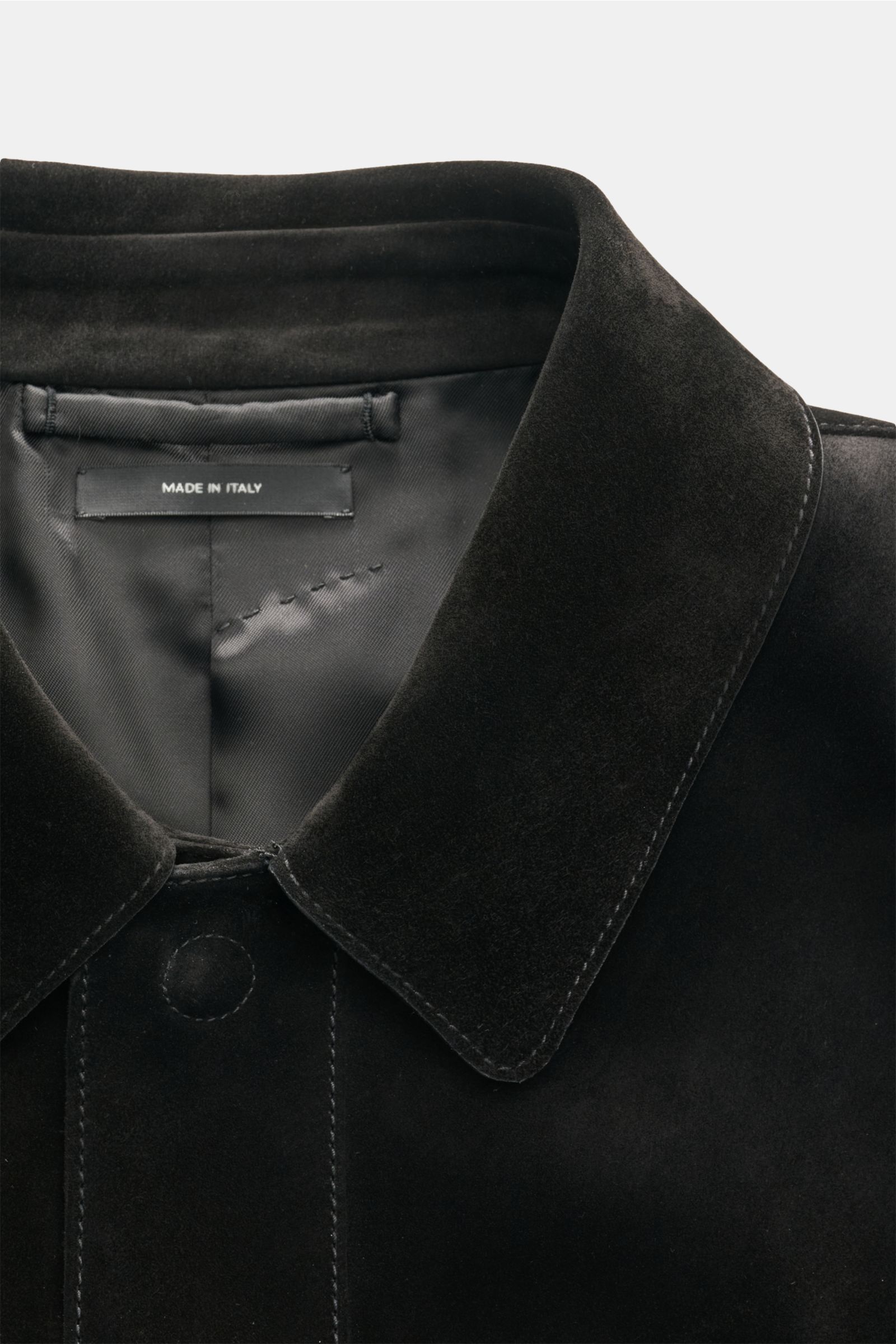 Close-up front view of Tom Ford Velourslederjacke schwarz collar and upper button area, made from finest black suede leather with smooth texture and visible stitching, featuring a hidden snap button placket and soft shiny interior lining, photographed fro