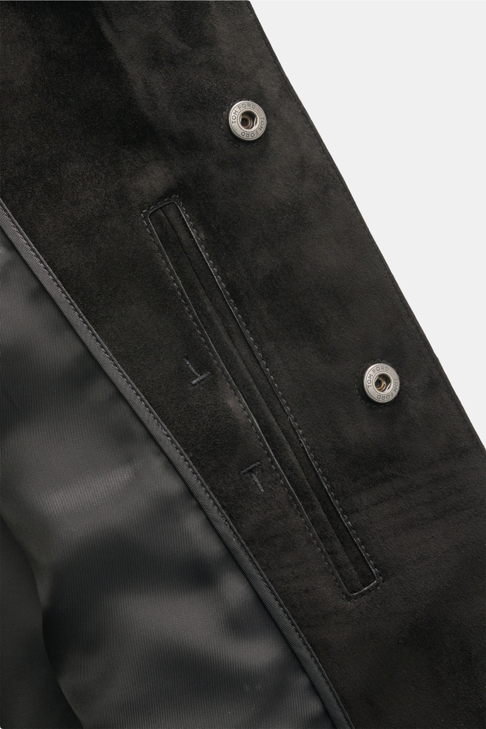 Close-up of the Tom Ford Velourslederjacke schwarz, showing the soft black suede material, snap buttons with logo, and sleek pocket detail from a top-down angle.