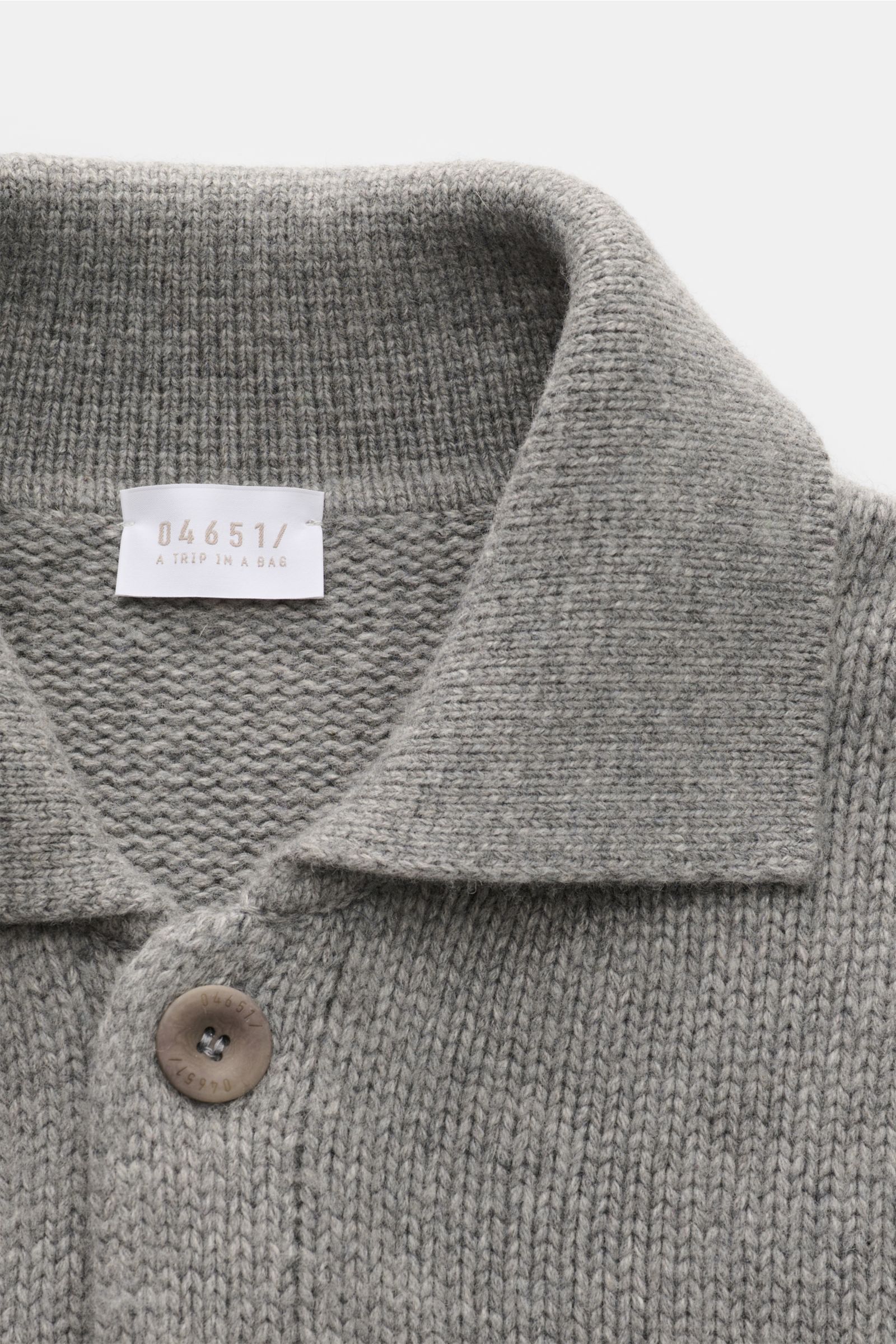 Graue Nahaufnahme aus schräger Perspektive des 04651/ A trip in a bag Cardigan 'Boiled Blouson' mit Umlegekragen, schwerem Strick und sichtbarem Knopf.