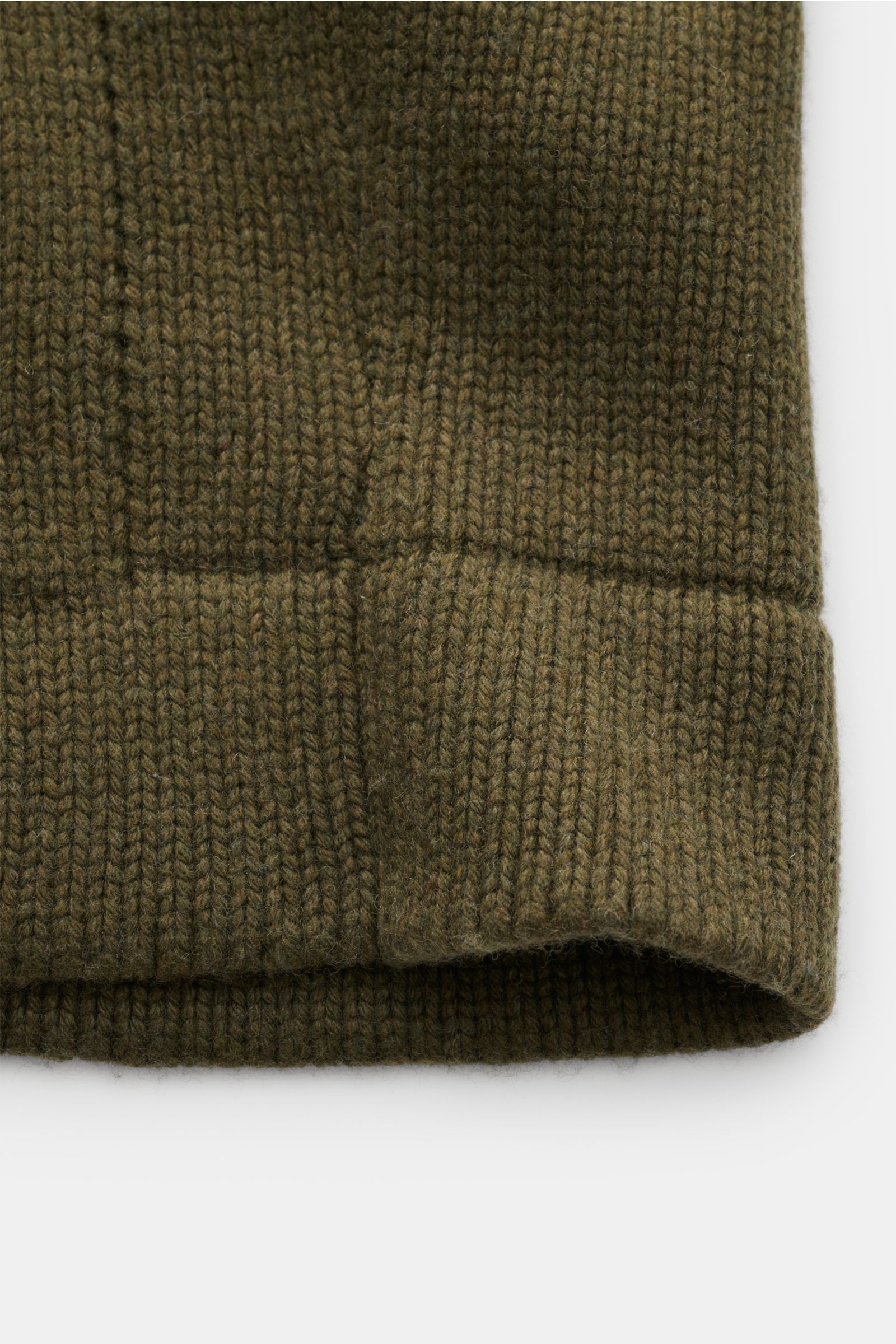 Close-up front view of the ribbed hem and angled hip pocket of the 04651/ A trip in a bag Cardigan 'Boiled Blouson' olive, a slim-fit wool blend cardigan with soft, heavy fabric and six-button placket.