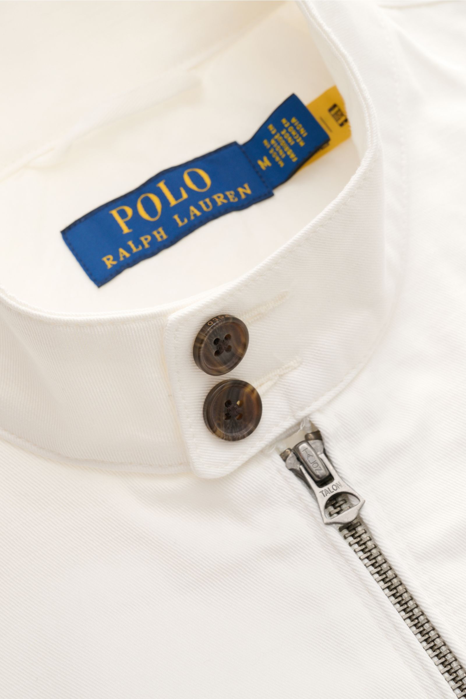 Polo Ralph Lauren Blouson weiß aus weichem Baumwolltwill, Detailaufnahme von Stehkragen mit Knöpfen und robustem Reißverschluss.