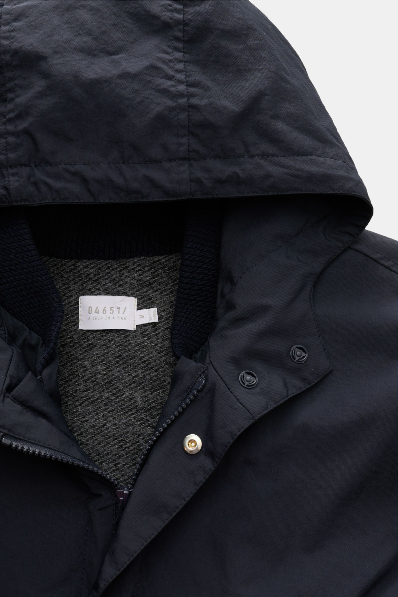 Close-up top-front view of the 04651/ A trip in a bag Parka 'The Triple' navy showing the hood, zip, storm flap with buttons, and textured contrasting lining. Lightweight and sporty for transitional weather, this parka features high-quality microfibre, a 
