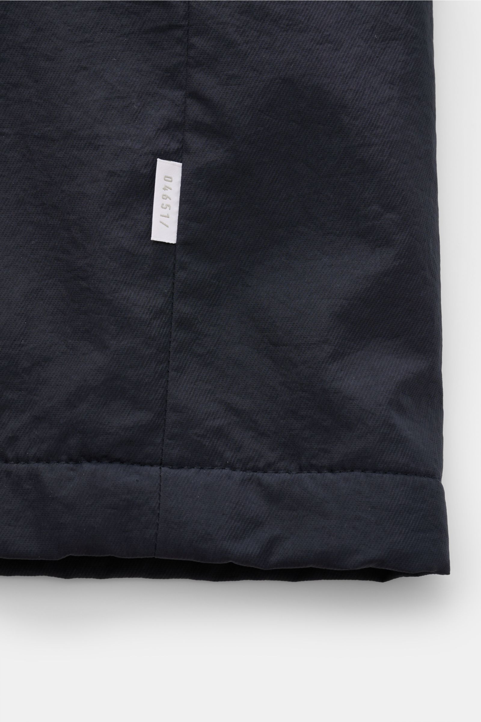 Close-up view of the lower hem of the 04651/ A trip in a bag Parka 'The Triple' navy, showing textured microfiber fabric and sewn-in logo label. Lightweight and sporty for the transitional period: This versatile parka with detachable gilet by 04651/ A TRI