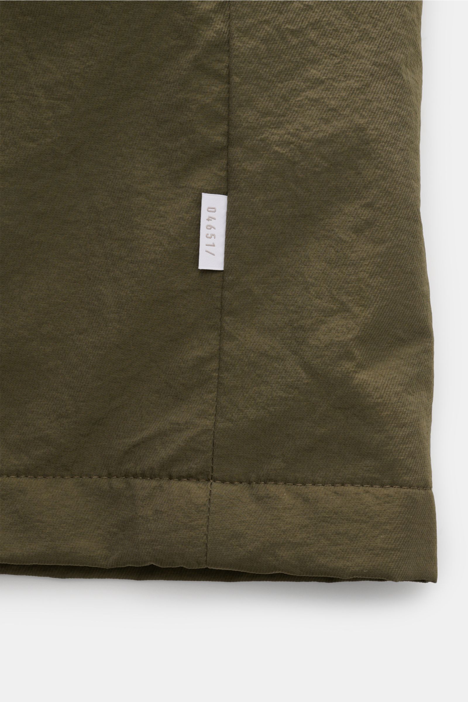 Close-up front view of the olive green 04651/ A trip in a bag Parka 'The Triple' oliv showing textured microfiber fabric and white logo label. Sportlich-leger durch die Übergangszeit: Der vielseitige Parka mit herausnehmbarer Weste von 04651/ A TRIP IN A 