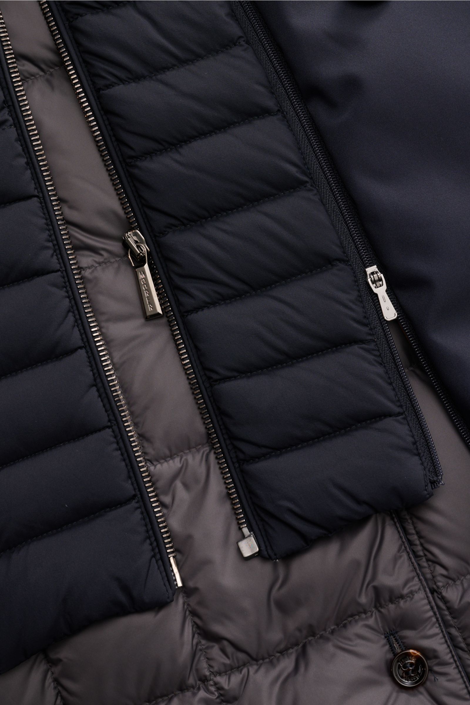 Close-up front view of Moorer Daunenjacke 'Bolgi' navy showing navy quilted outer fabric with silver zippers and smooth grey inner lining.

The provided HTML content describes the jacket as follows:

Eleganz trifft Funktion: Gefertigt aus edlem Gabardine 