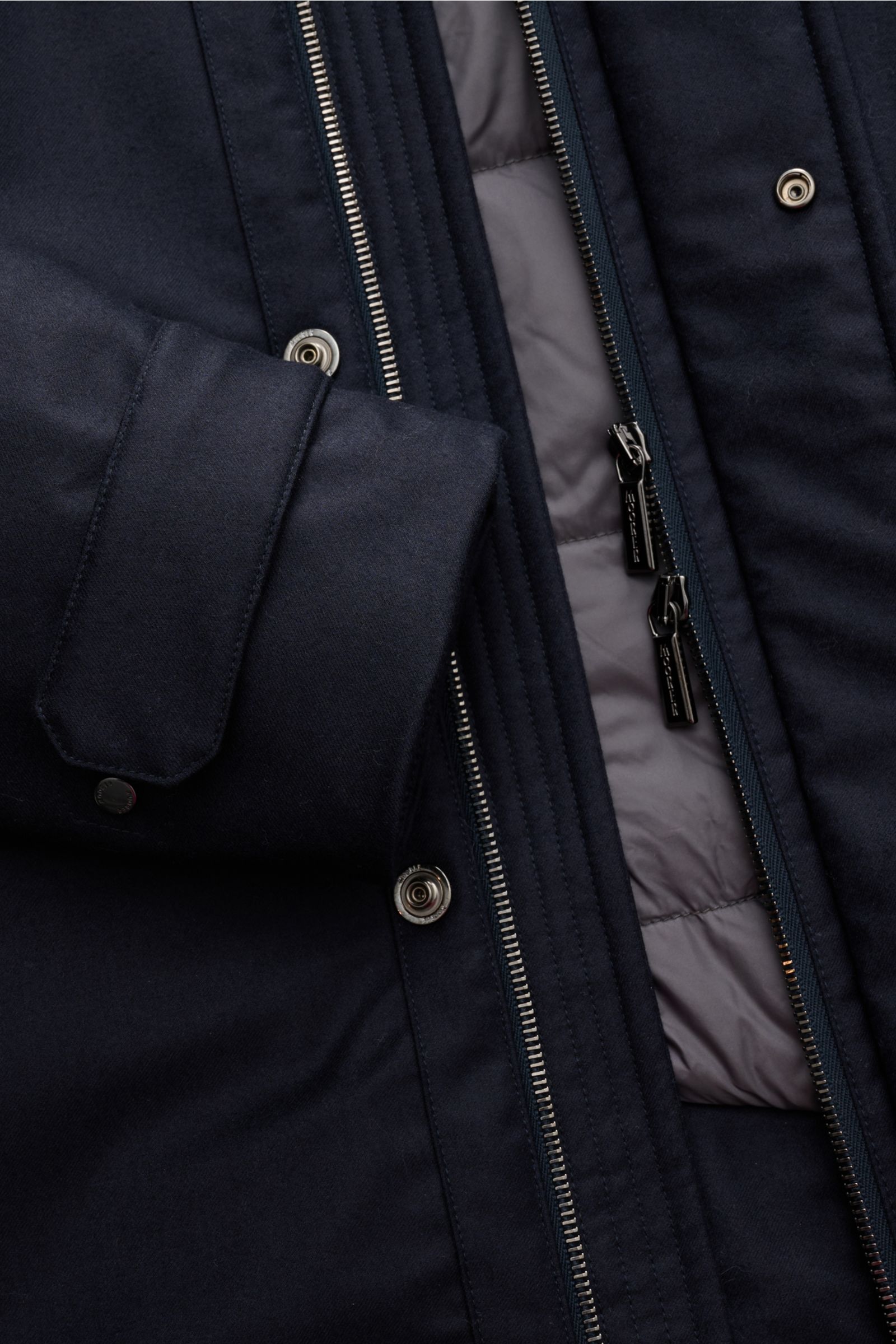 Nahaufnahme des Moorer Daunenparka 'Vido' dark navy von vorne, zeigt wasserabweisende Woll-Cashmere-Mischung, Daunenfüllung, zwei-Wege-Reißverschluss, Druckknöpfe und Ärmelabschluss.