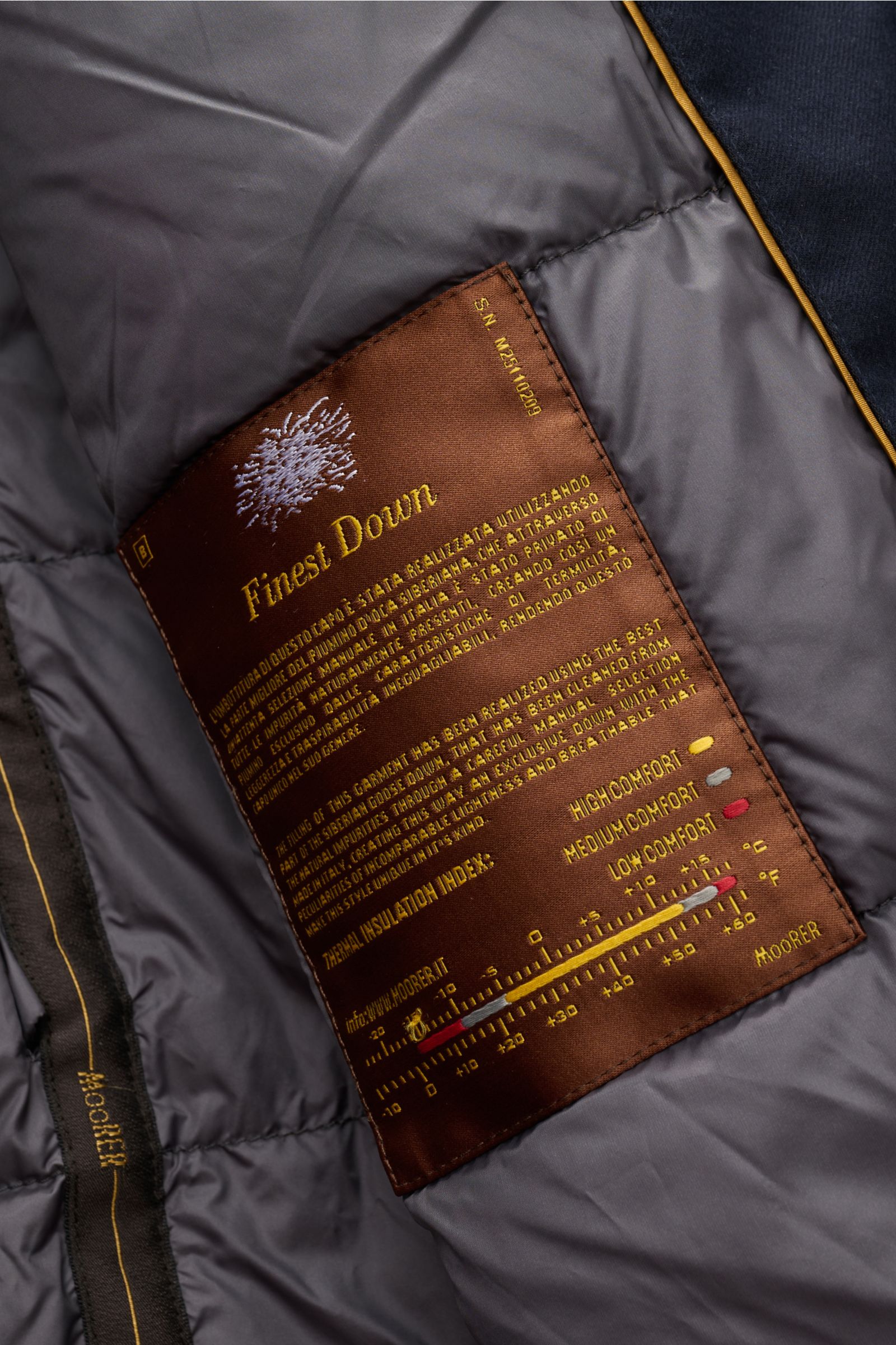 Nahaufnahme des Innenfutters mit braunem „Finest Down“-Label im Moorer Daunenparka 'Vido' dark navy, Detailansicht von schräg oben.