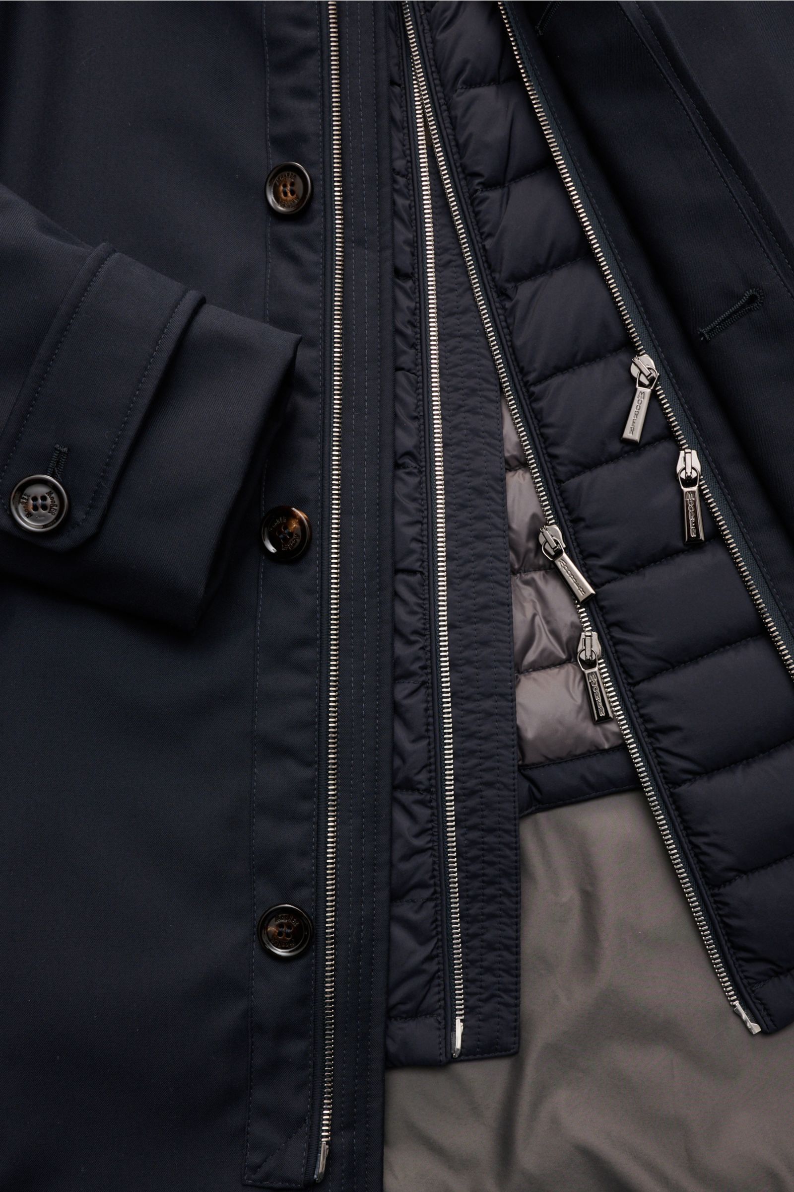 Nahaufnahme des geöffneten Moorer Kurzmantels 'Elson' navy, zeigt außen wind- und wasserabweisenden Stoff, herausnehmbare Daunenjacke, zwei Wege Reißverschlüsse, Knöpfe und Manschetten mit Knopf.