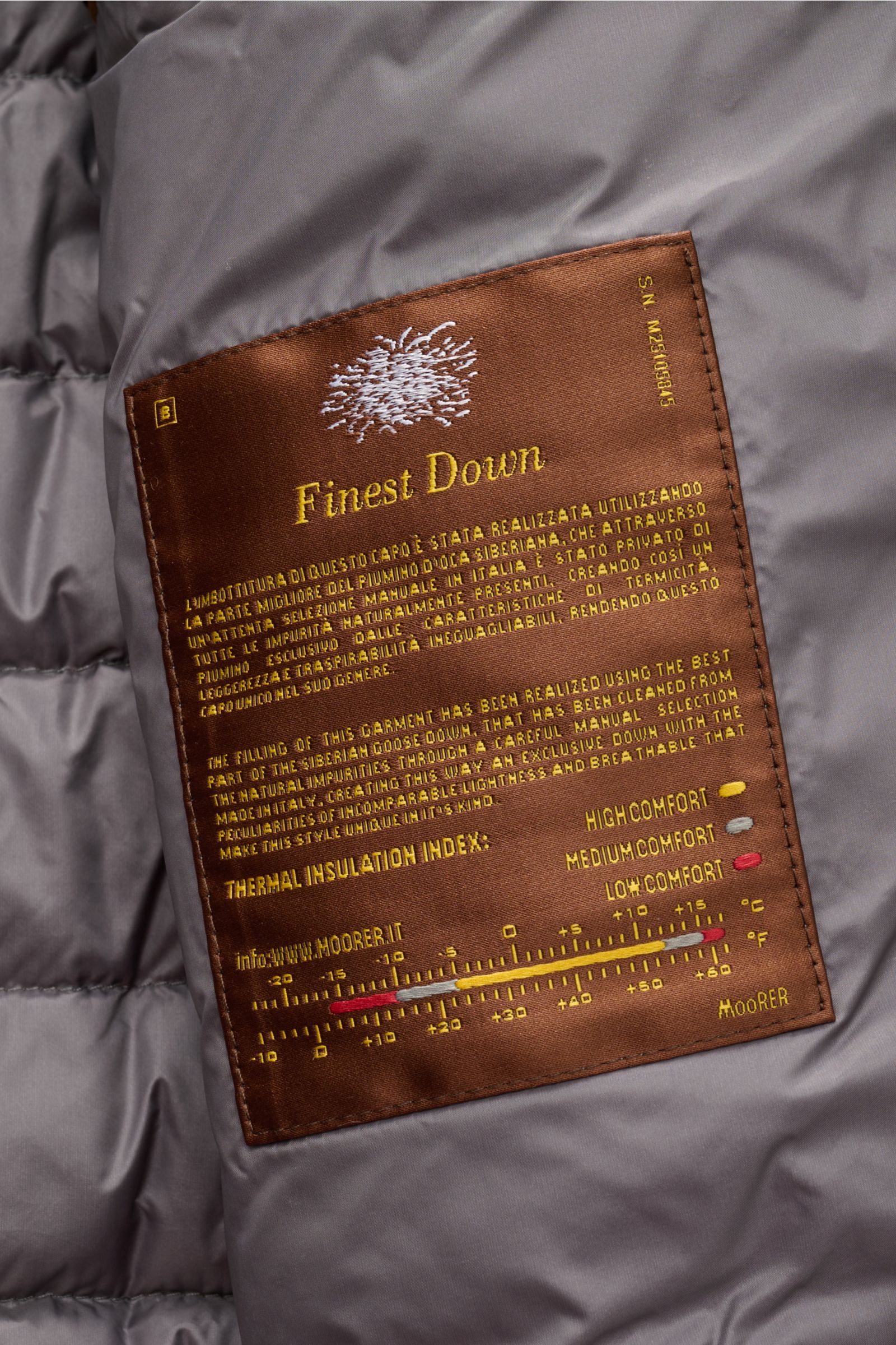 Nahaufnahme des braunen Labels im Innenfutter des Moorer Daunenblouson 'Oniro' grau, das die leichte Daunenfüllung und Komforteigenschaften beschreibt.