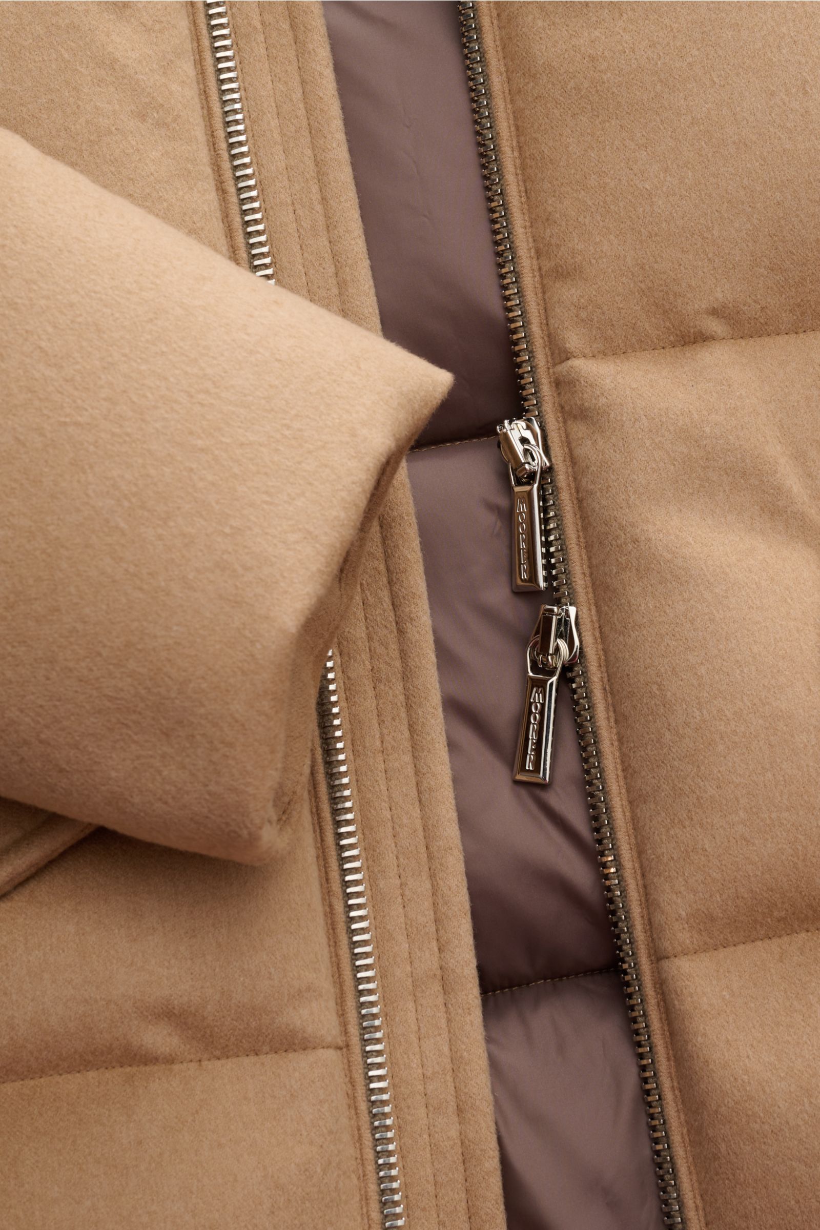 Nahaufnahme der geöffneten Moorer Daunenjacke 'Valls' camel von vorne, mit sichtbarem Zwei-Wege-Reißverschluss, weichem Kamelhaar und wattiertem Innenfutter.