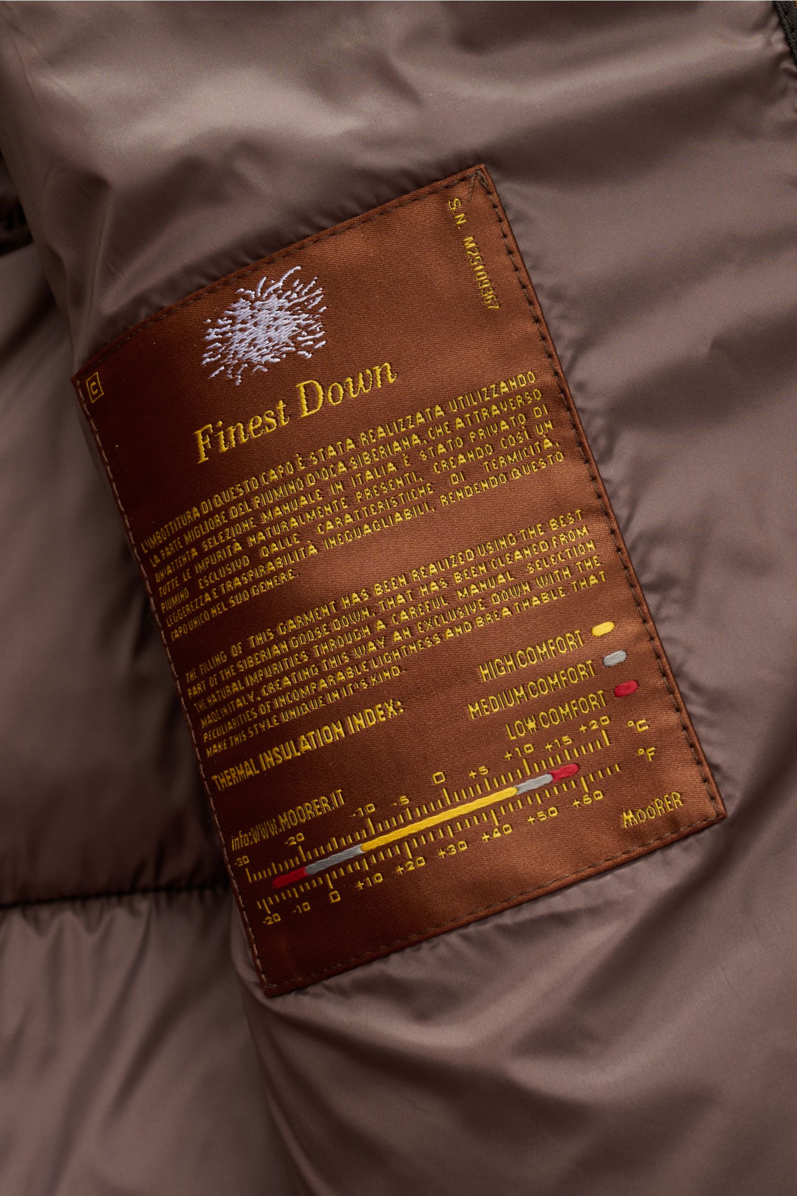 Nahaufnahme des Innenfutters der Moorer Daunenjacke 'Valls' camel mit braunem Finest Down-Label, weich, thermoregulierend, wind- und wasserabweisend.