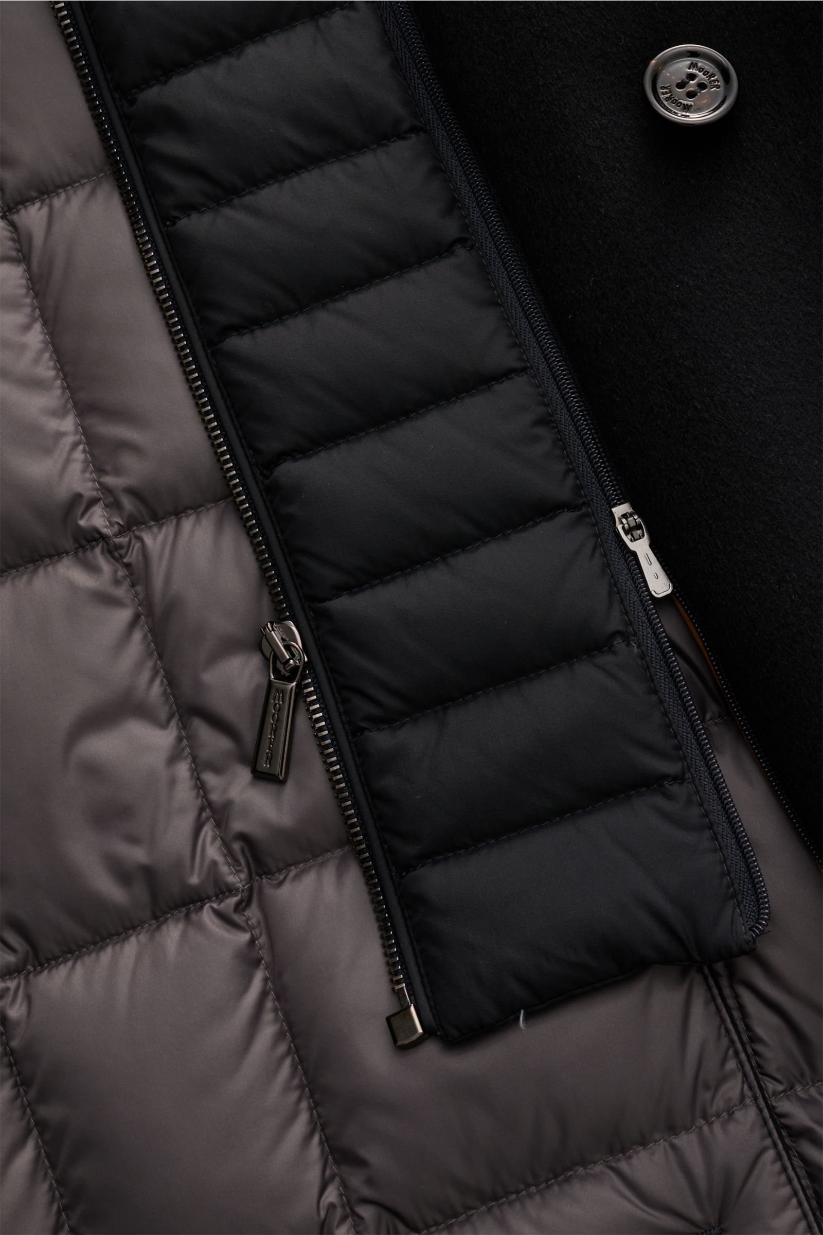 Close-up view of the inner lining and zippers of the Moorer Jacke 'Volmer-Kn' navy, showing quilted water-repellent fabric and button detail.

Die 'Volmer-Kn' von MOORER vereint stilvolle Eleganz mit praktischer Funktionalität. Im Cabanjacken-Stil geha