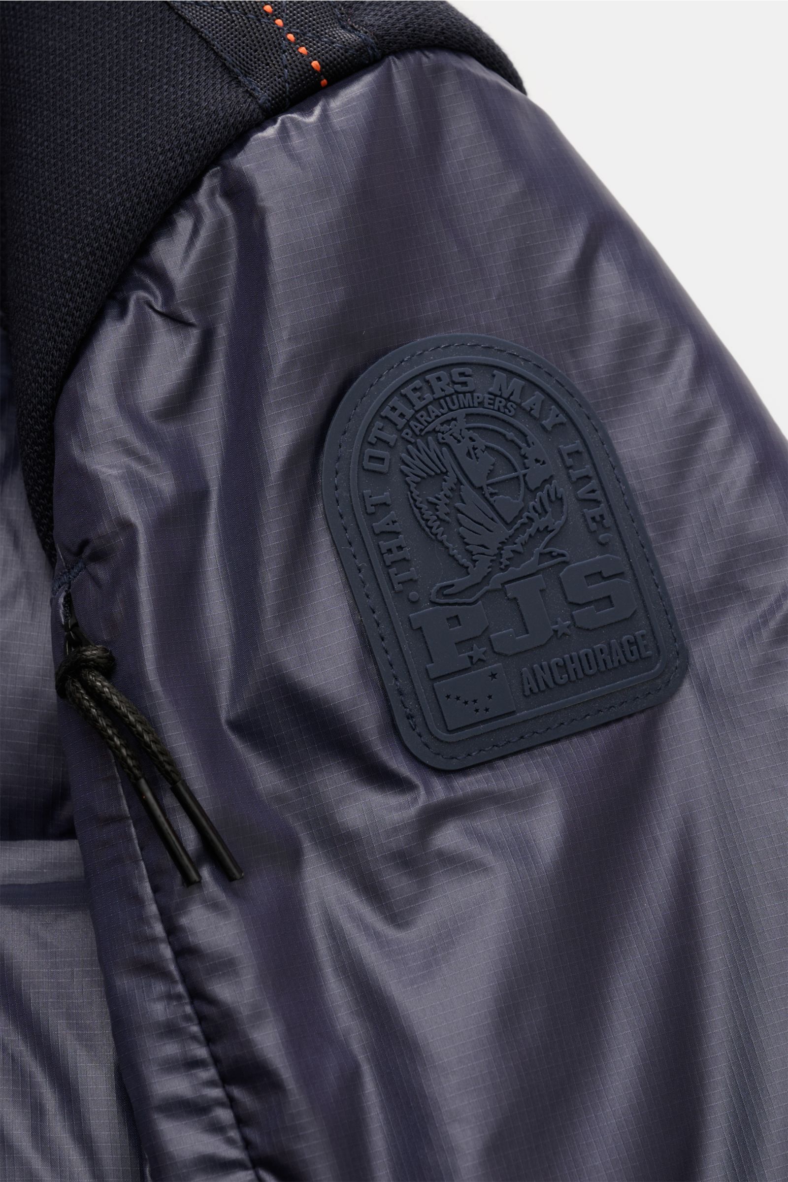 Close-up side view of the Parajumpers Daunenjacke 'Gyles' navy showing the shiny ripstop microfibre with robust jersey details, the gummiertes PARAJUMPERS patch, and zipper pull cords, highlighting the quilted design and fine texture. Für einen sportiven 