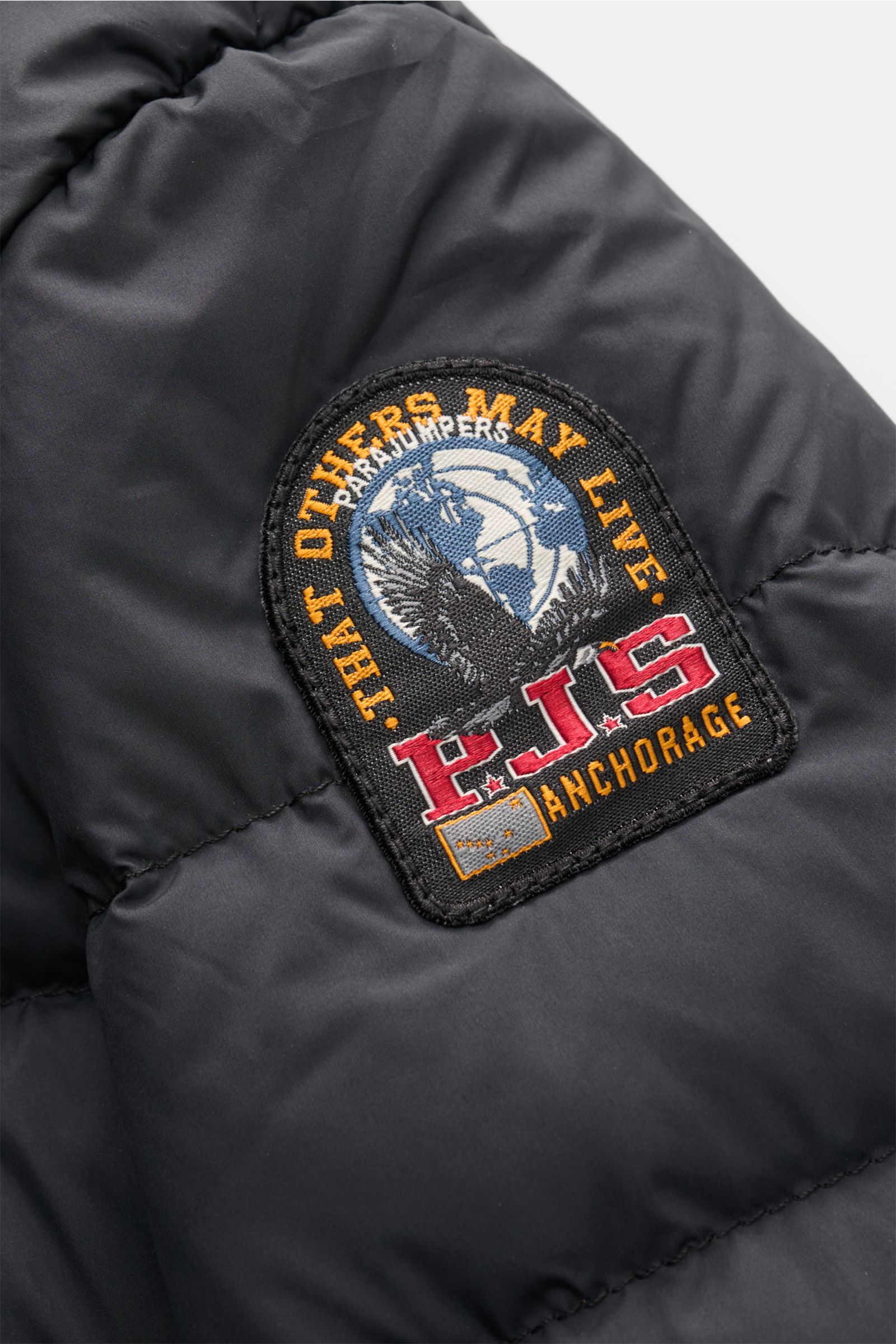 Nahaufnahme der schwarzen Parajumpers Daunenjacke 'Ugo' mit Fokus auf dem detailreichen, bestickten Weblabel am Oberarm, gefertigt aus strapazierfähiger Microfaser und ultraleichter, nachhaltiger Daunenfüllung.