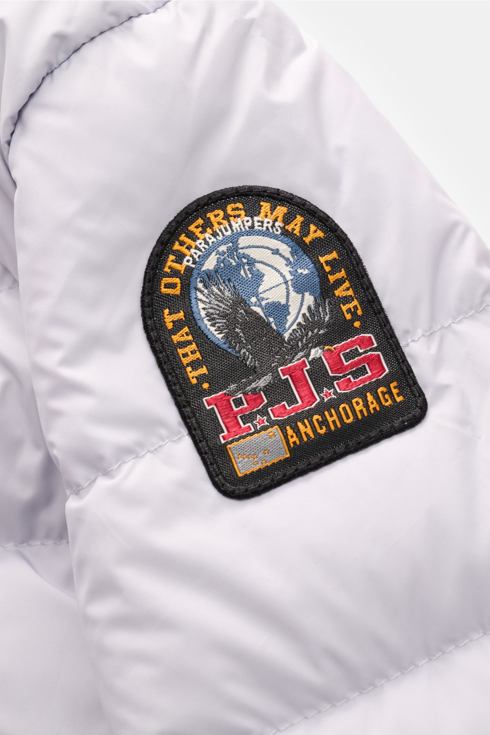 Parajumpers Daunenjacke 'Ugo' hellgrau shown in close-up from the side, featuring a detailed embroidered patch with eagle and text. Lässiges Design und ein klares Statement für Nachhaltigkeit: Die Jacke 'Ugo' von PARAJUMPERS sorgt mit ultraleichter Daunen