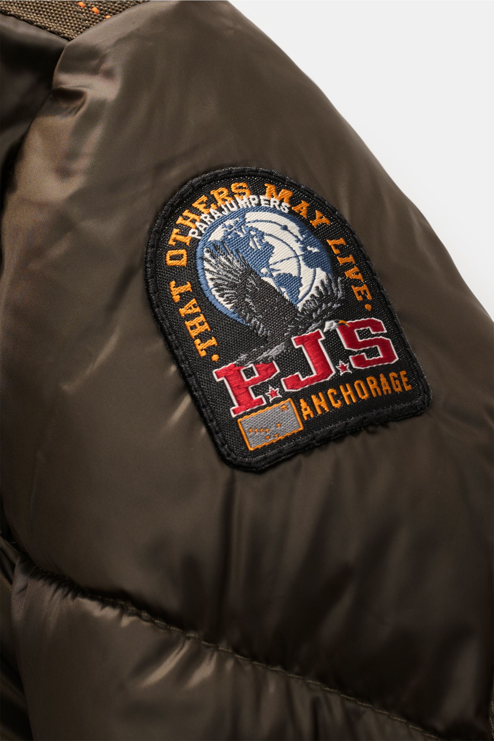 Nahaufnahme des Parajumpers Daunenblouson 'Pharrell' dark olive von schräg oben, zeigt das PJS-Logo, strapazierfähige Microfaser und leichte Daunenfüllung.