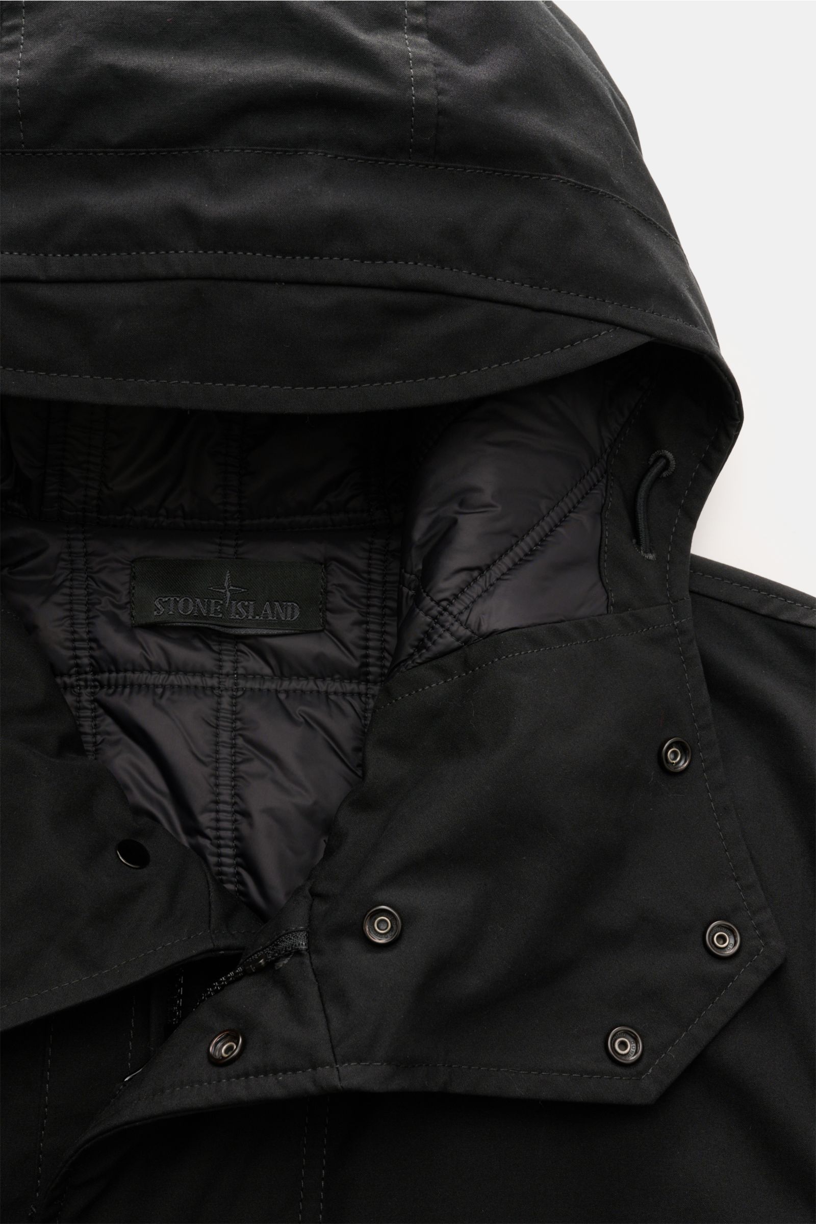 Nahaufnahme der Stone Island Jacke 'Weatherproof Cotton Canvas Ghost Piece' schwarz, von oben fotografiert, mit Kapuze, wind- und wasserabweisendem Baumwoll-Canvas und gesteppter Innenfütterung.