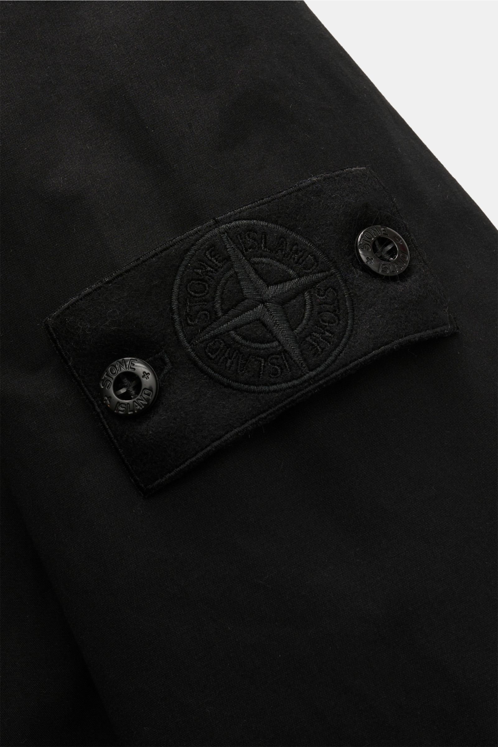 Nahaufnahme des schwarzen Kompass-Badges an der Stone Island Jacke 'Weatherproof Cotton Canvas Ghost Piece' aus dicht gewebtem Baumwoll-Canvas.