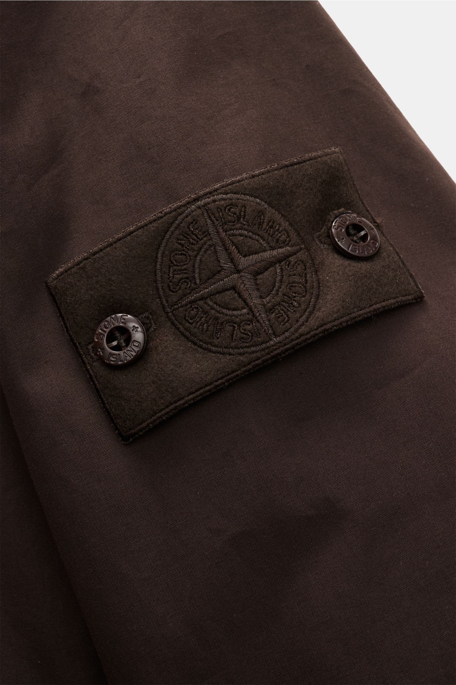 Stone Island Jacke 'Weatherproof Cotton Canvas Ghost Piece' dunkelbraun, Detailaufnahme des Kompass-Badges aus dicht gewebtem Baumwoll-Canvas.