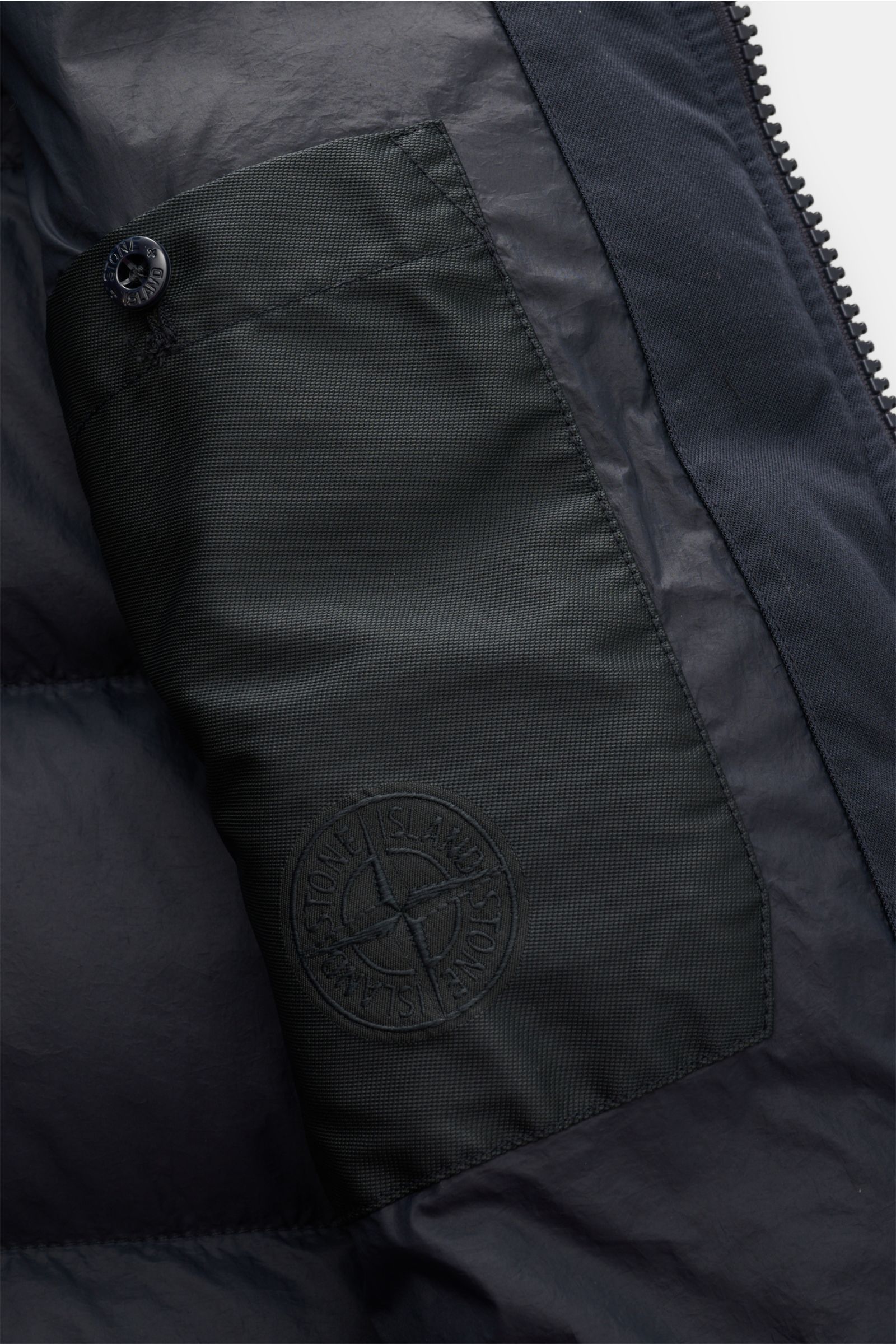 Close-up interior view of the Stone Island Daunenjacke 'Twill Wool-TC Ghost Piece' navy showing the black textured inner pocket with embossed logo and button. Monochromes Statement-Piece für die Übergangszeit: Die Daunenjacke aus der 'Ghost' Kollektion vo