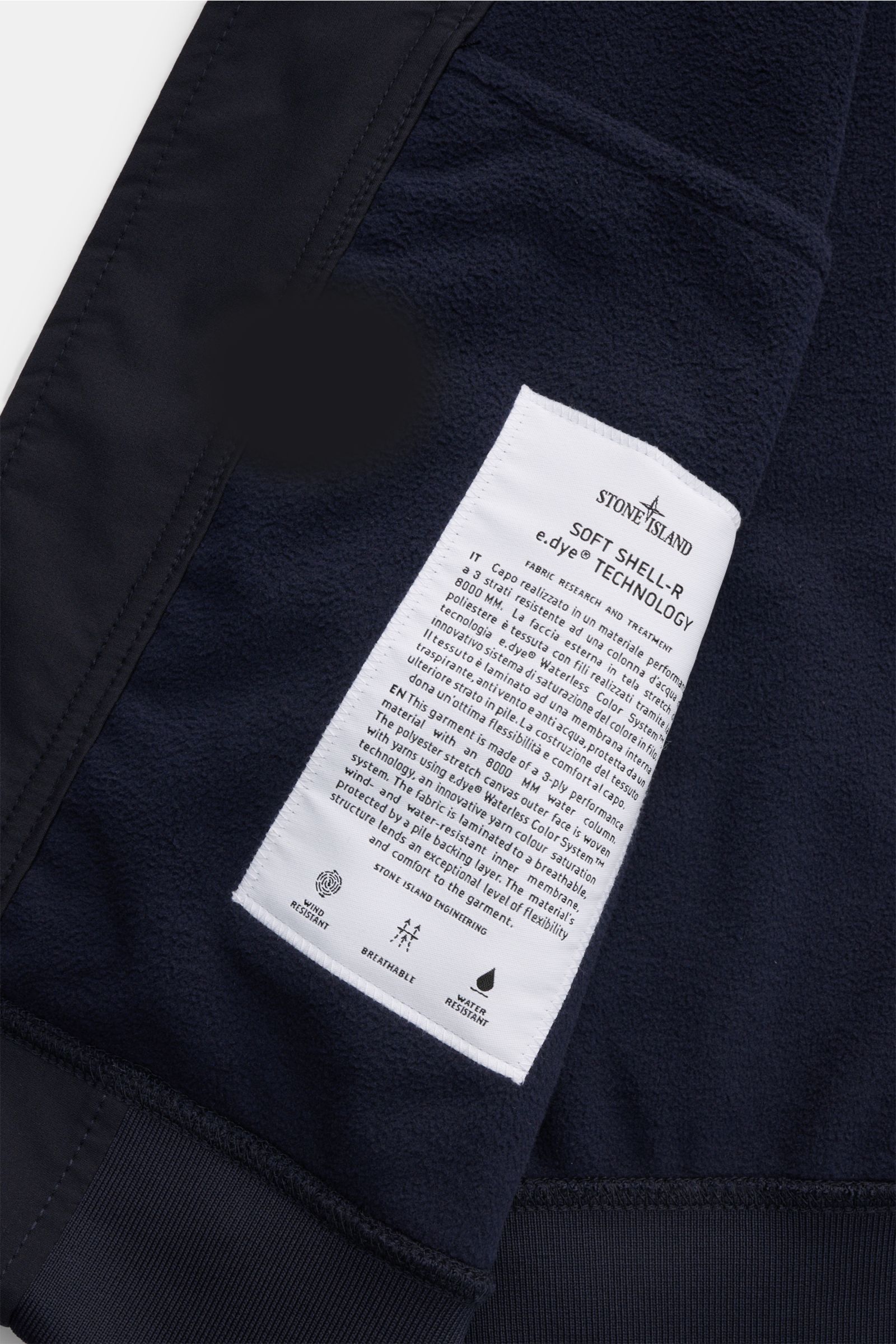 Close-up inside view of Stone Island Softshell-Blouson 'Light Soft Shell-R e.dye Technology' navy showing the white care label on navy elastic microfiber fabric with ribbed cuffs, featuring wind- and water-repellent, breathable, slim fit design.

Ob fü