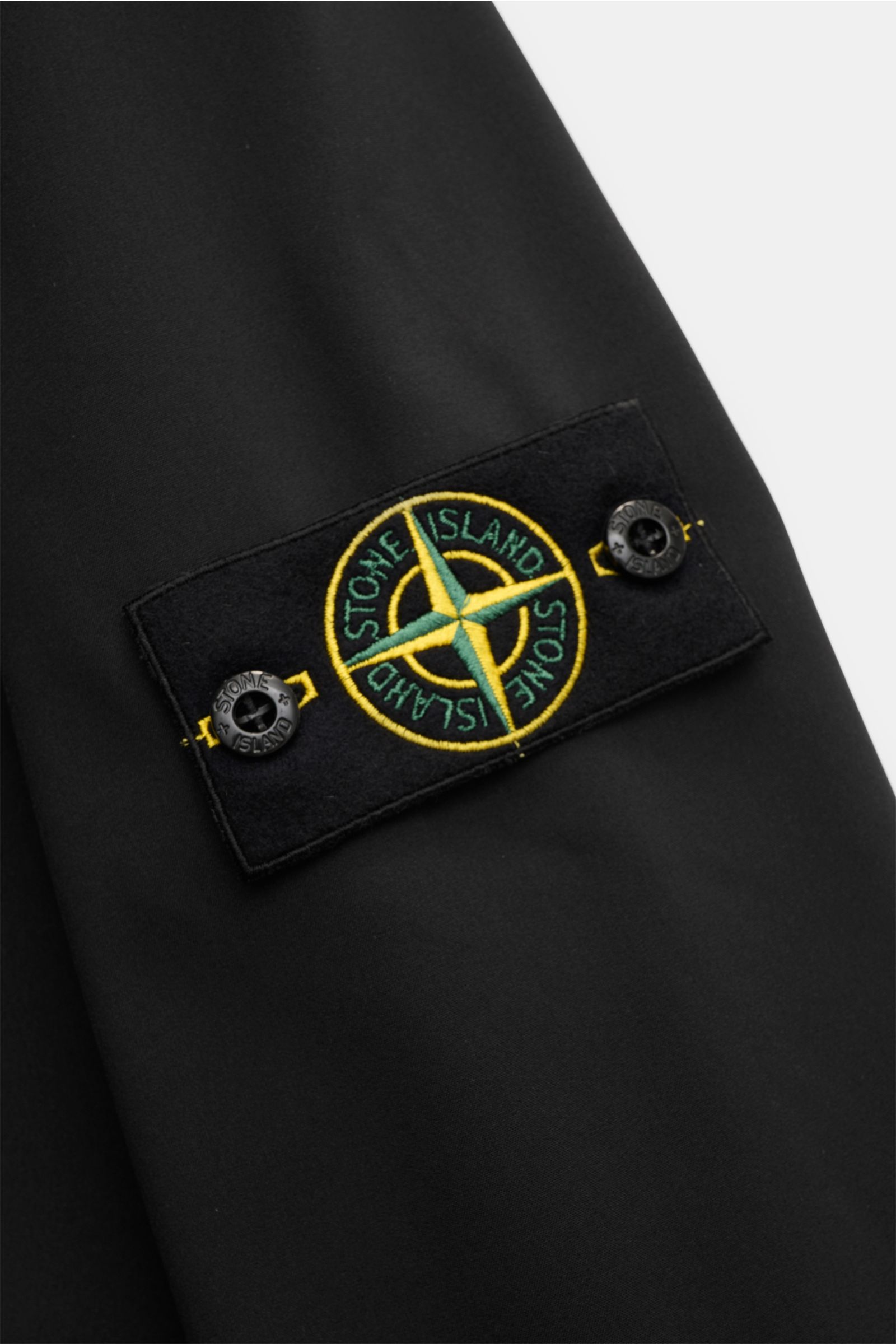 Close-up view of the Stone Island Softshell-Blouson 'Light Soft Shell-R e.dye Technology' schwarz showing the black fabric and distinctive compass badge on the sleeve. Ob für sportliche Aktivitäten oder als Casual-Allrounder, auf die wind- und wasserab