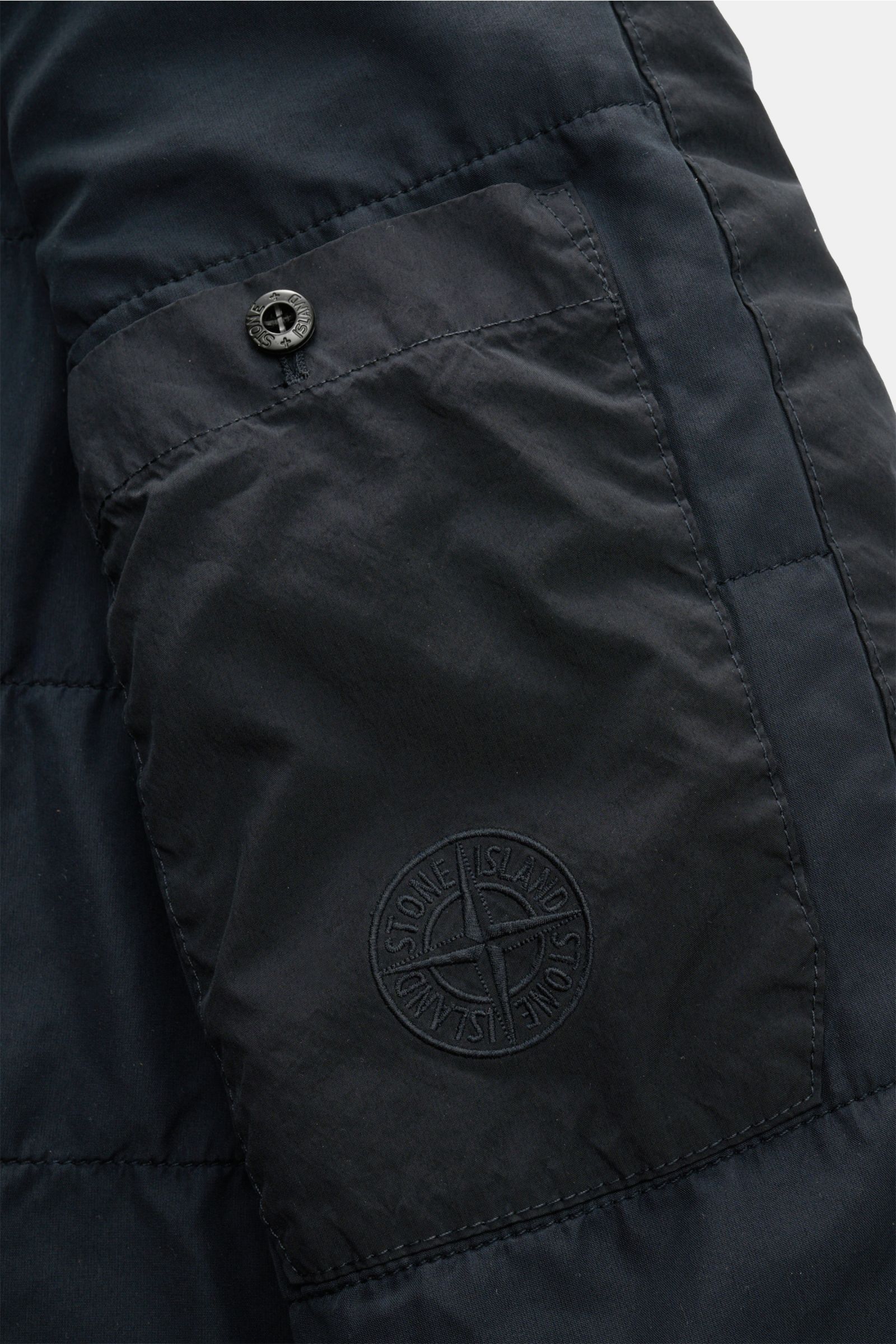 Stone Island Jacke 'Light Compact Touch Poly-TC' navy, Detailaufnahme der wasserabweisenden elastischen Microfaser mit Kompass-Badge am Ärmel, schräge Pattentasche mit Druckknopf.