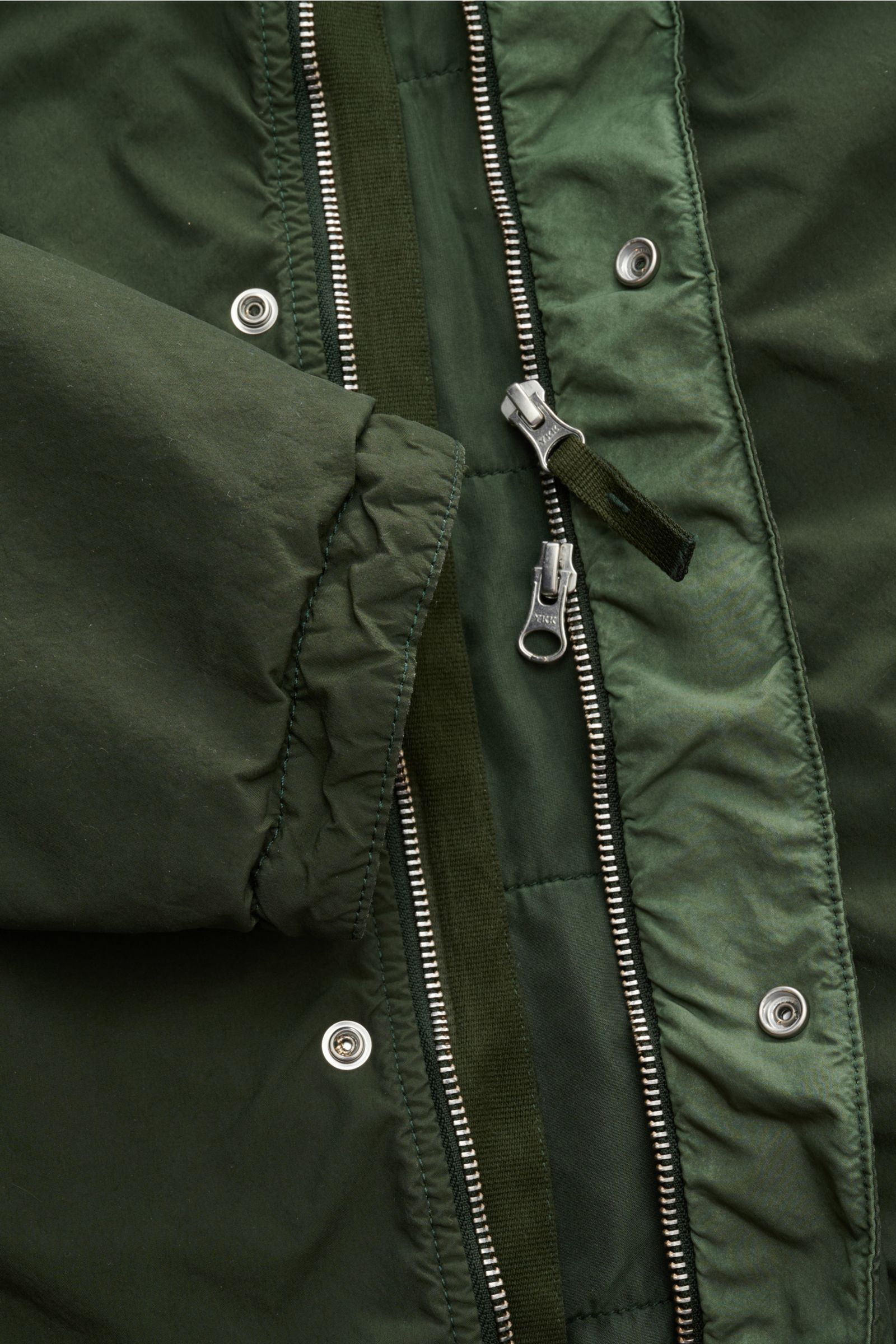 Stone Island Jacke 'Light Compact Touch Poly-TC' dunkelgrün, Detailansicht von innen mit Reißverschluss, Druckknöpfen und elastischem Ärmelabschluss.