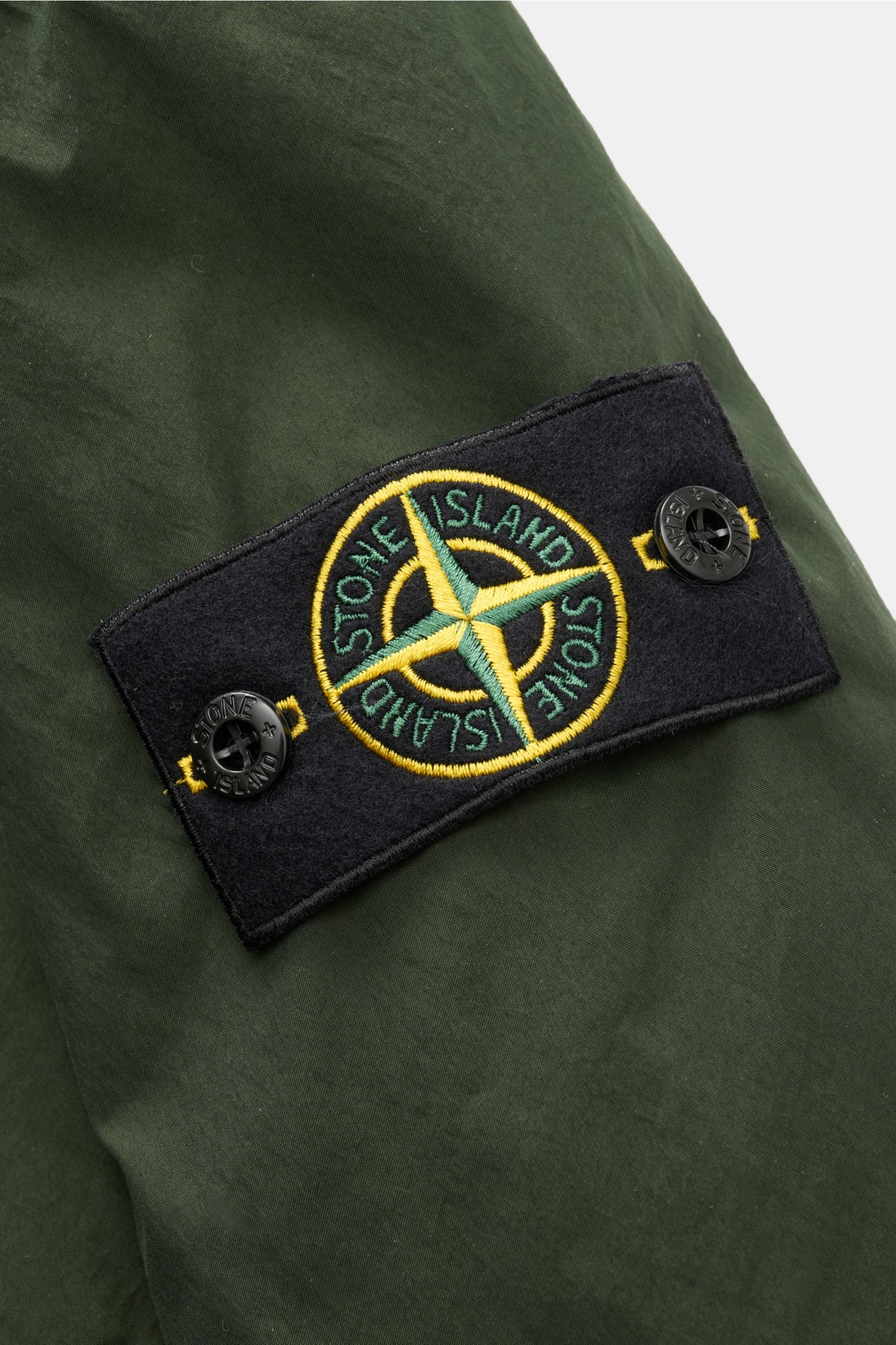 Stone Island Jacke 'Light Compact Touch Poly-TC' dunkelgrün im Detail, Nahaufnahme des typischen Kompass-Badges am Ärmel, elastische Microfaser, wasserabweisend, garment dyed.