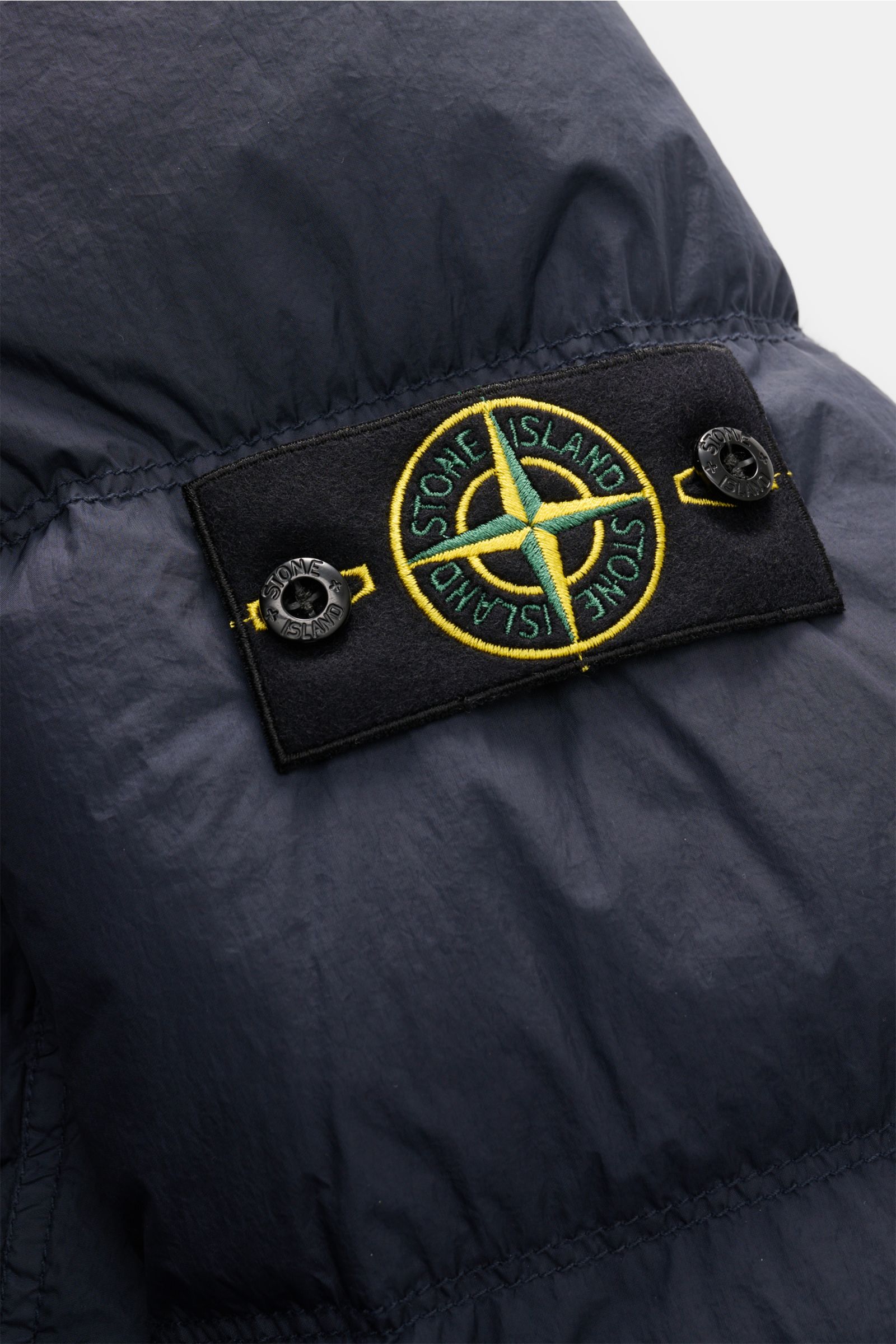 Close-up of the Stone Island Daunenjacke 'Garment Dyed Crinkle Reps NY' navy showing the embroidered compass badge on the sleeve, photographed from a detailed side angle. Bei der Daunenjacke 'Garment Dyed Crinkle Reps NY' von STONE ISLAND trifft beschicht
