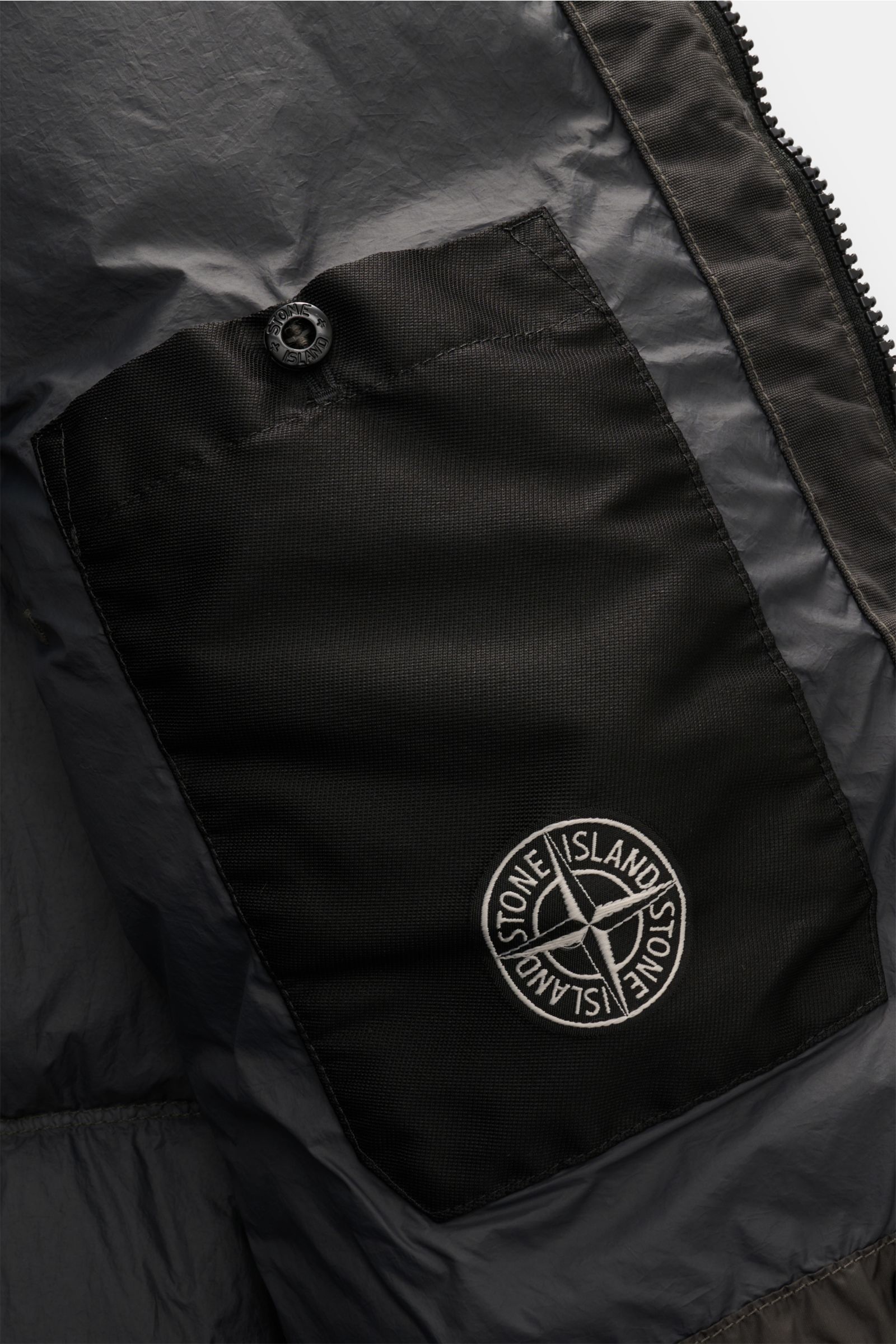 Innenansicht der Stone Island Daunenjacke 'Garment Dyed Crinkle Reps NY' dunkelgrau mit Innentasche und Kompass-Badge, Detailaufnahme.