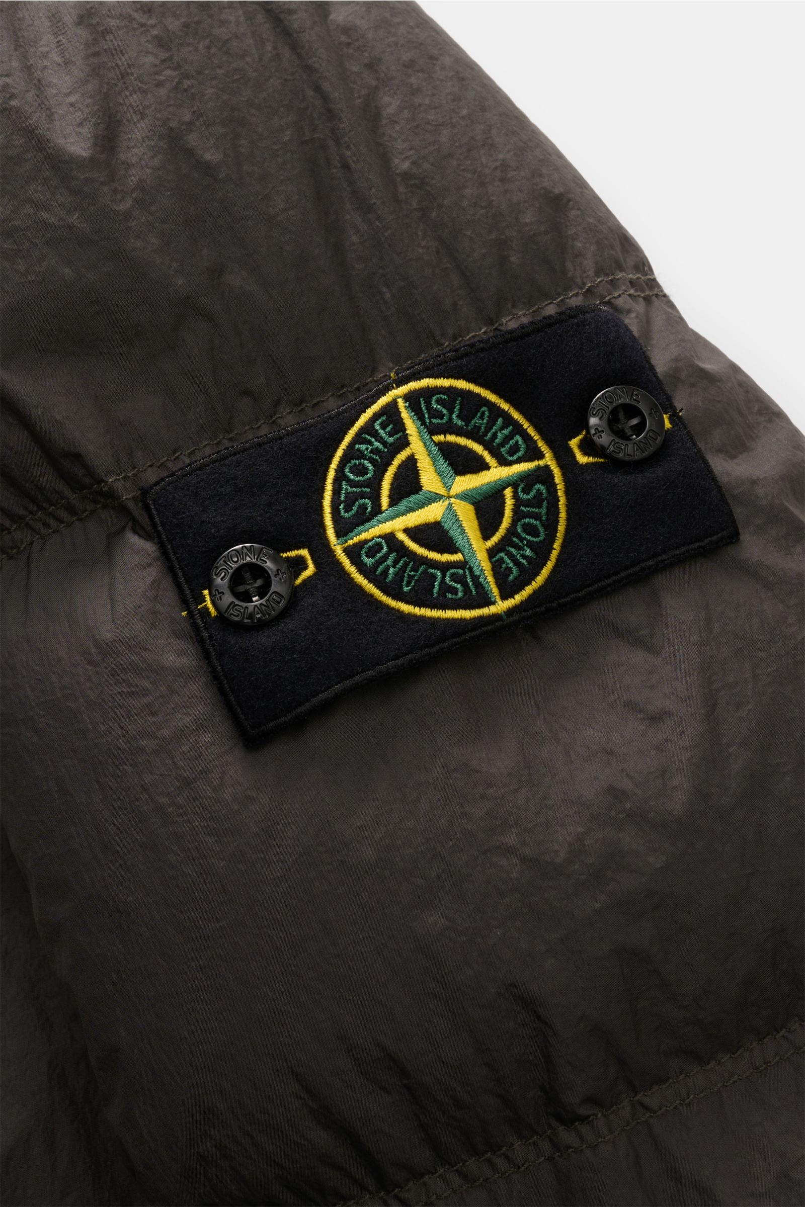 Stone Island Daunenjacke 'Garment Dyed Crinkle Reps NY' dunkelgrau, Detailaufnahme des typischen Kompass-Badges aus der Nahaufnahme, Crinkle-Microfaser.