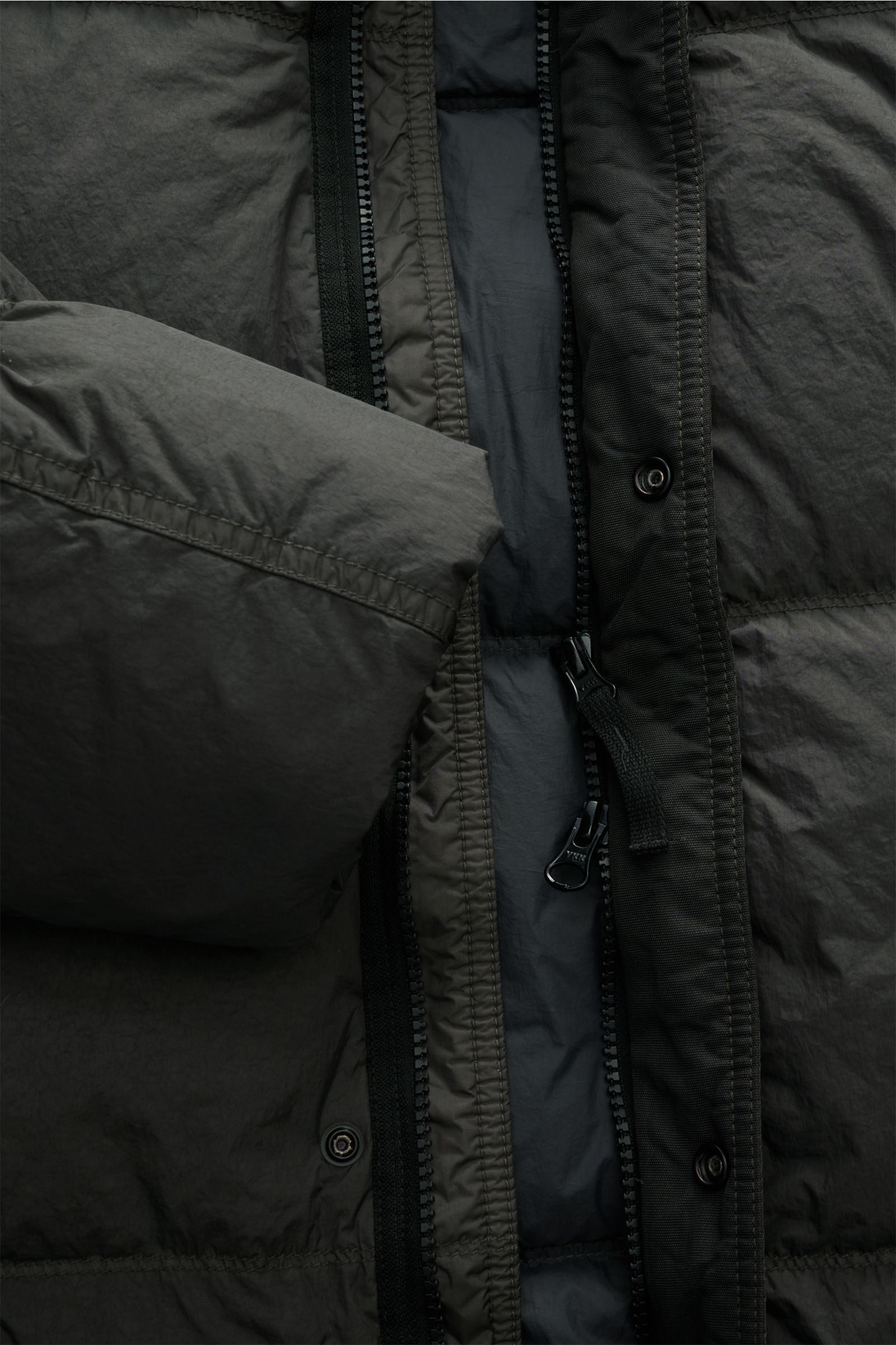 Close-up front view of Stone Island Daunenjacke 'Garment Dyed Crinkle Reps NY' dunkelgrau showing coated microfiber fabric, zipper, snap buttons, and padded down filling. The jacket features a garment-dyed crinkle look with wind- and water-resistant quali