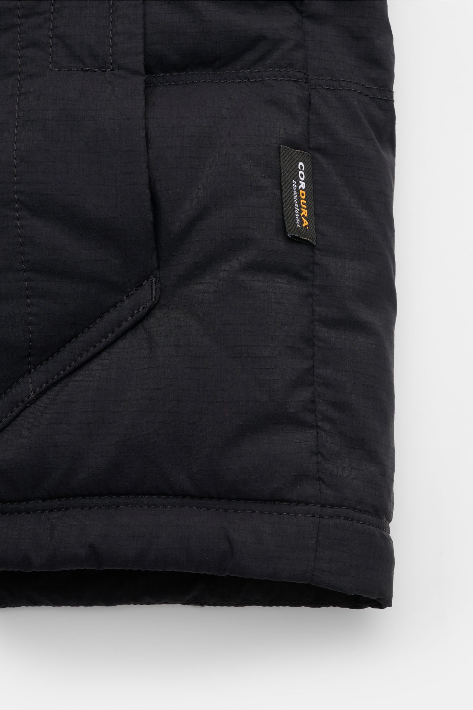Close-up side view of Stone Island Daunenjacke 'Matt Ripstop Cordura' navy showing black ripstop fabric, stitched details, and CORDURA® tag, highlighting its durable, wind- and water-resistant microfibre material with a soft touch and slim fit design. Leg