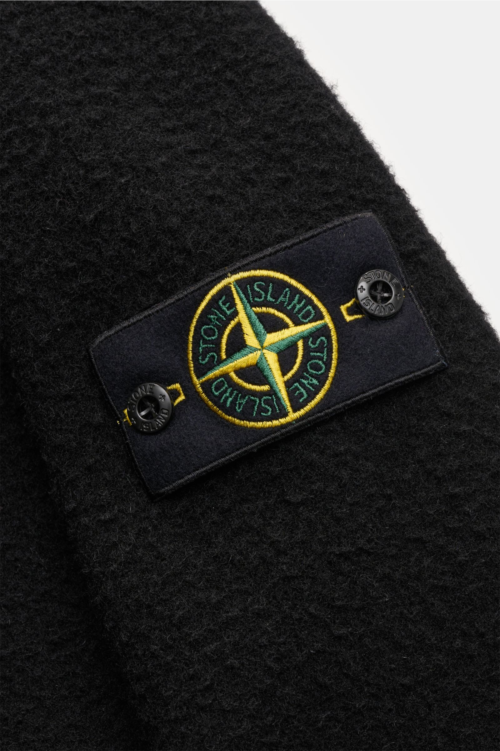 Close-up angled view of the Stone Island Blouson 'Panno Ratinato' schwarz showing its black textured wool-mix fabric and the iconic compass badge. Monochrome Herbst-Looks: Der Blouson 'Panno Ratinato' von STONE ISLAND wird mit seinem sportiven Design und 