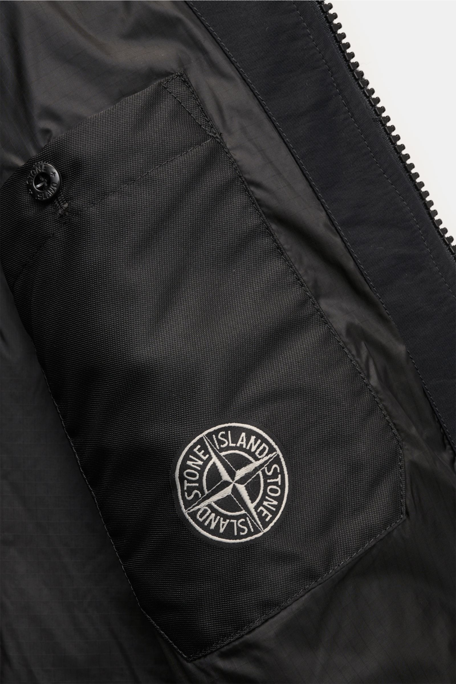 Close-up inside view of the Stone Island Blouson 'Panno Ratinato' schwarz showing the black inner pocket with the compass badge and zipper detail.

Monochrome Herbst-Looks: Der Blouson 'Panno Ratinato' von STONE ISLAND wird mit seinem sportiven Design 