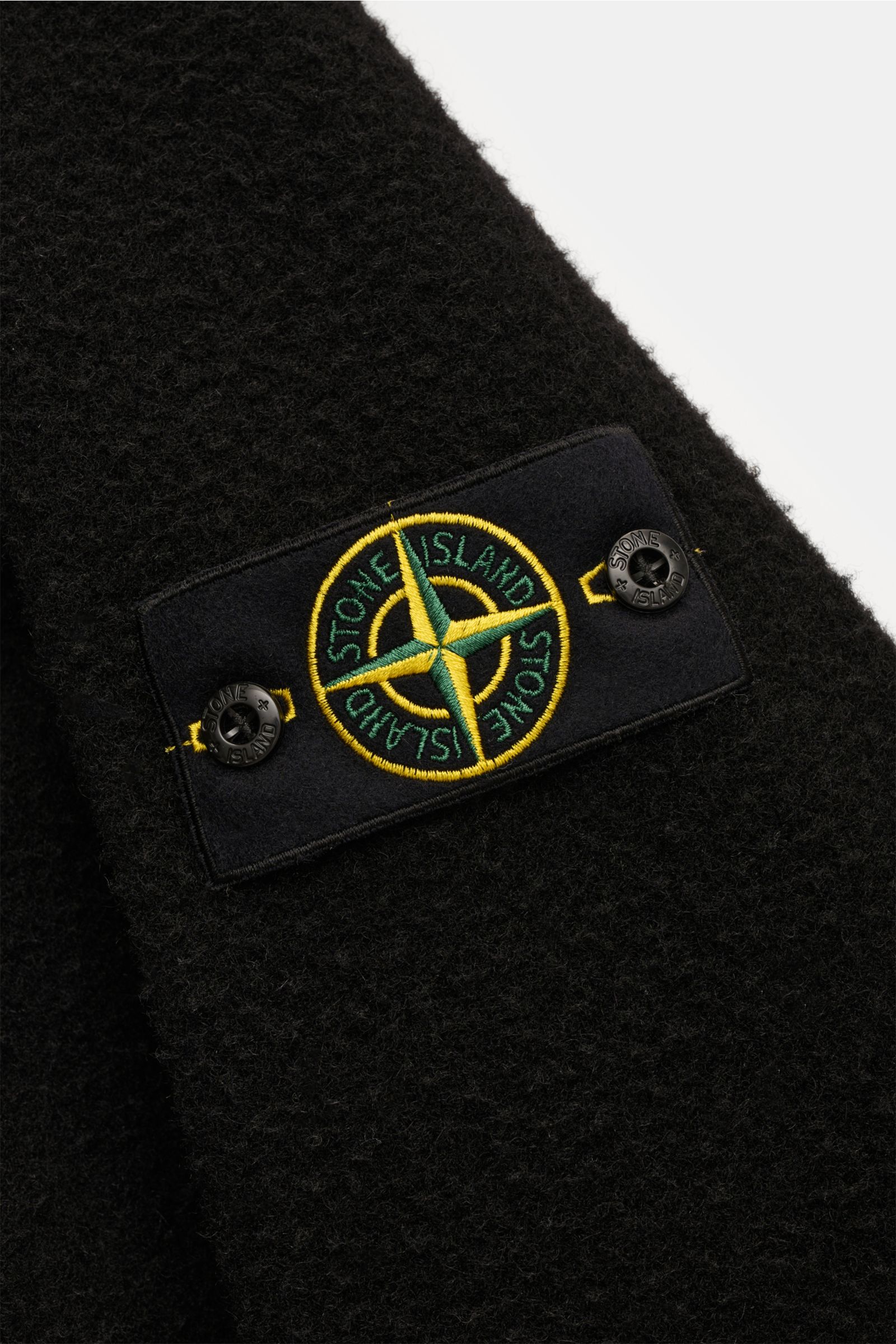 Close-up angled view of the Stone Island Jacket 'Panno Ratinato' black showing the textured ratiné finish and embroidered logo patch on the sleeve. Functional and eye-catching: This STONE ISLAND hooded jacket is an eye-catching, sporty piece for the colde